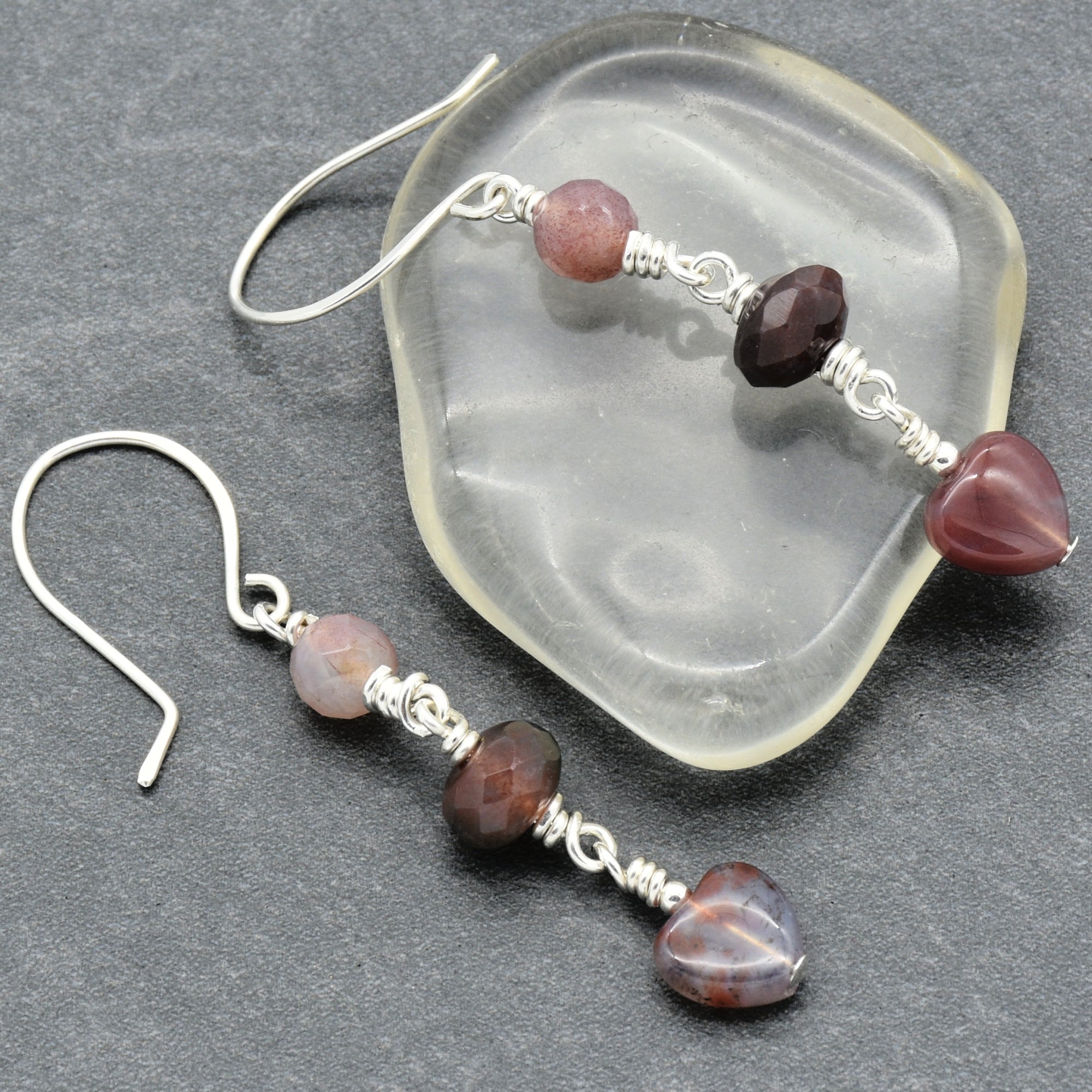 This image shows a pair of earrings. They have a hook design, with beads and a heart-shaped bead at the end.