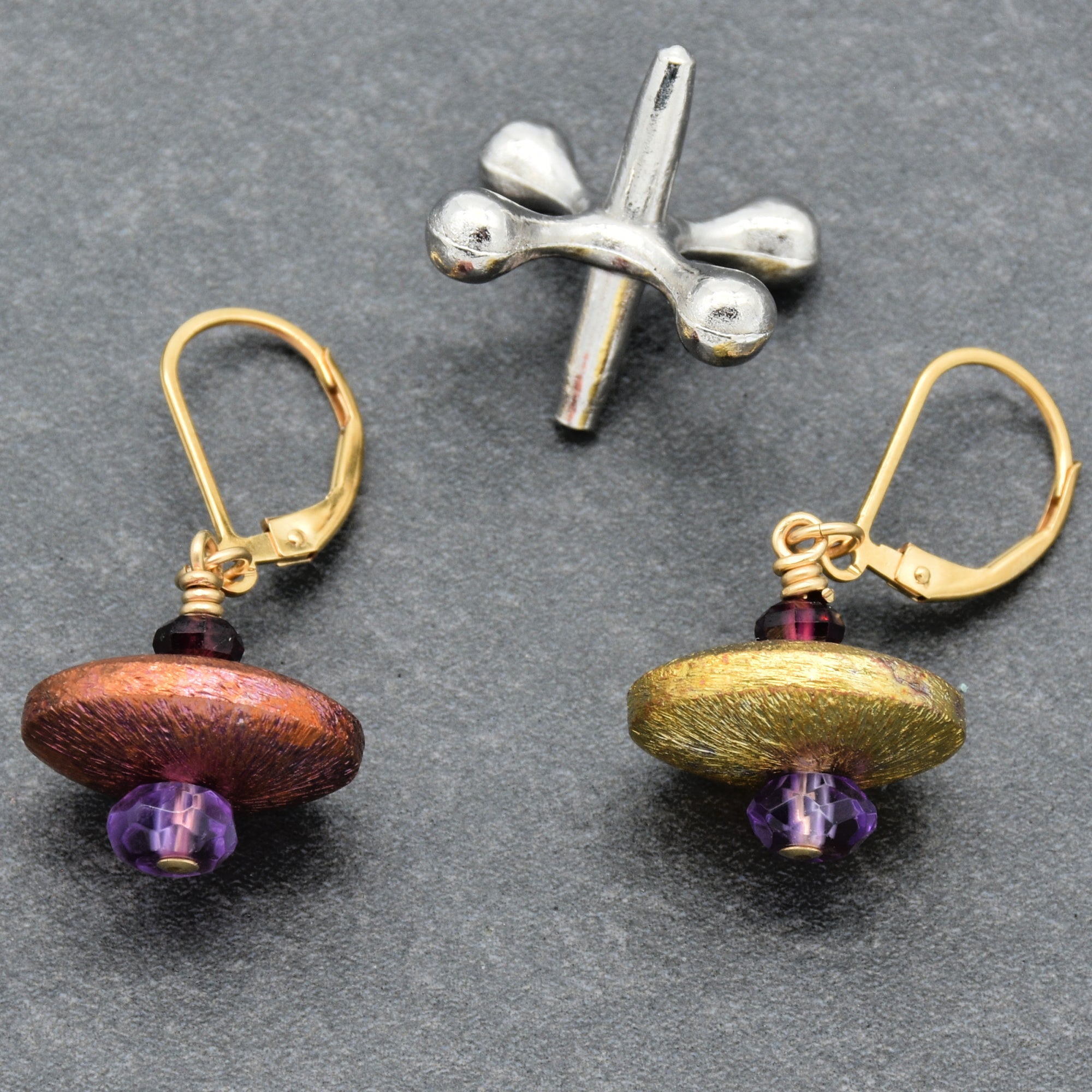 This image shows a pair of earrings. The items have ear hooks typically used for earrings, and the design includes beads, which is common for earrings. The metallic piece above them appears to be an unrelated object and not part of the jewelry set.