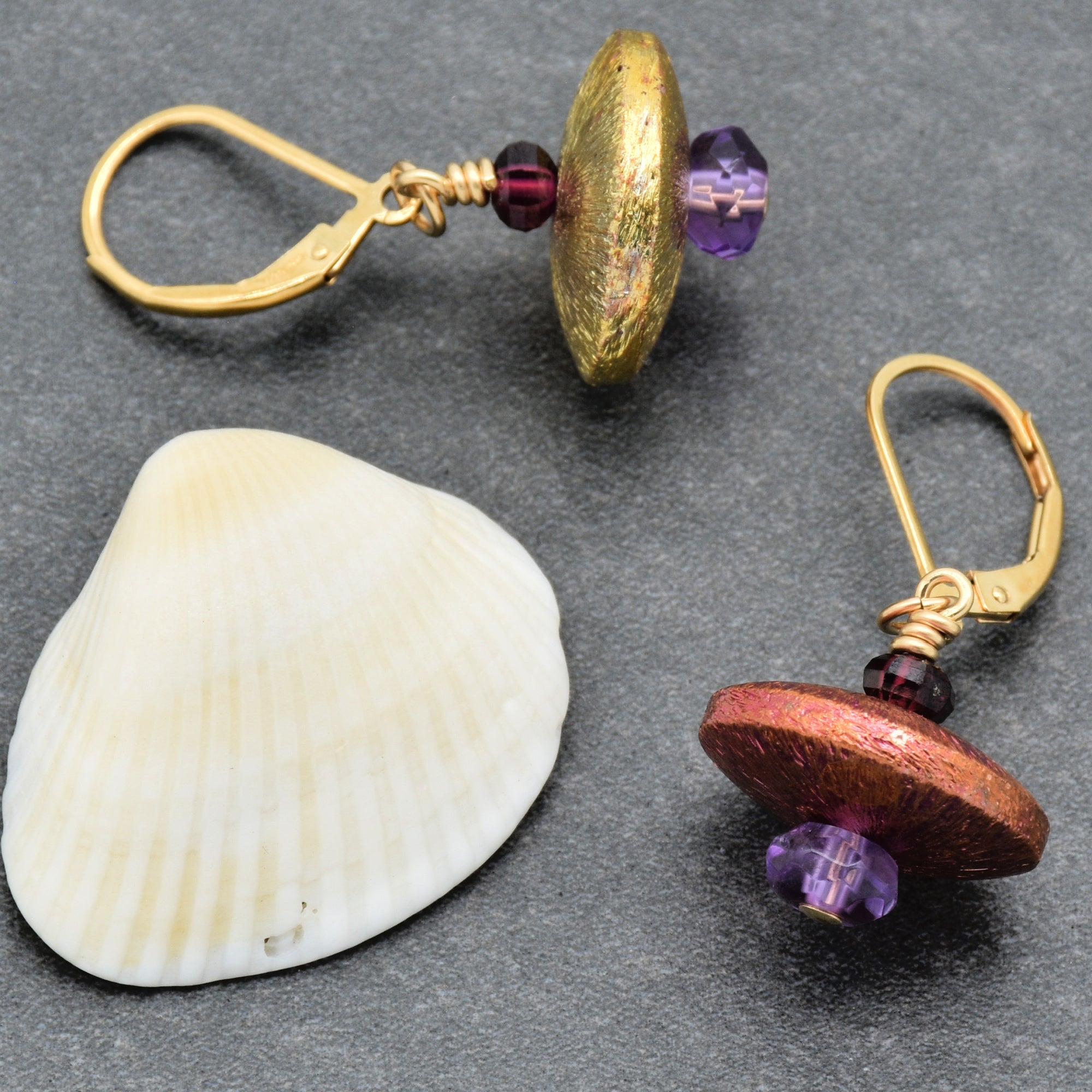 The image shows a pair of earrings. They have gold-colored hooks and decorative beads in purple and reddish-gold tones. The jewelry pieces are not a necklace or a bracelet.