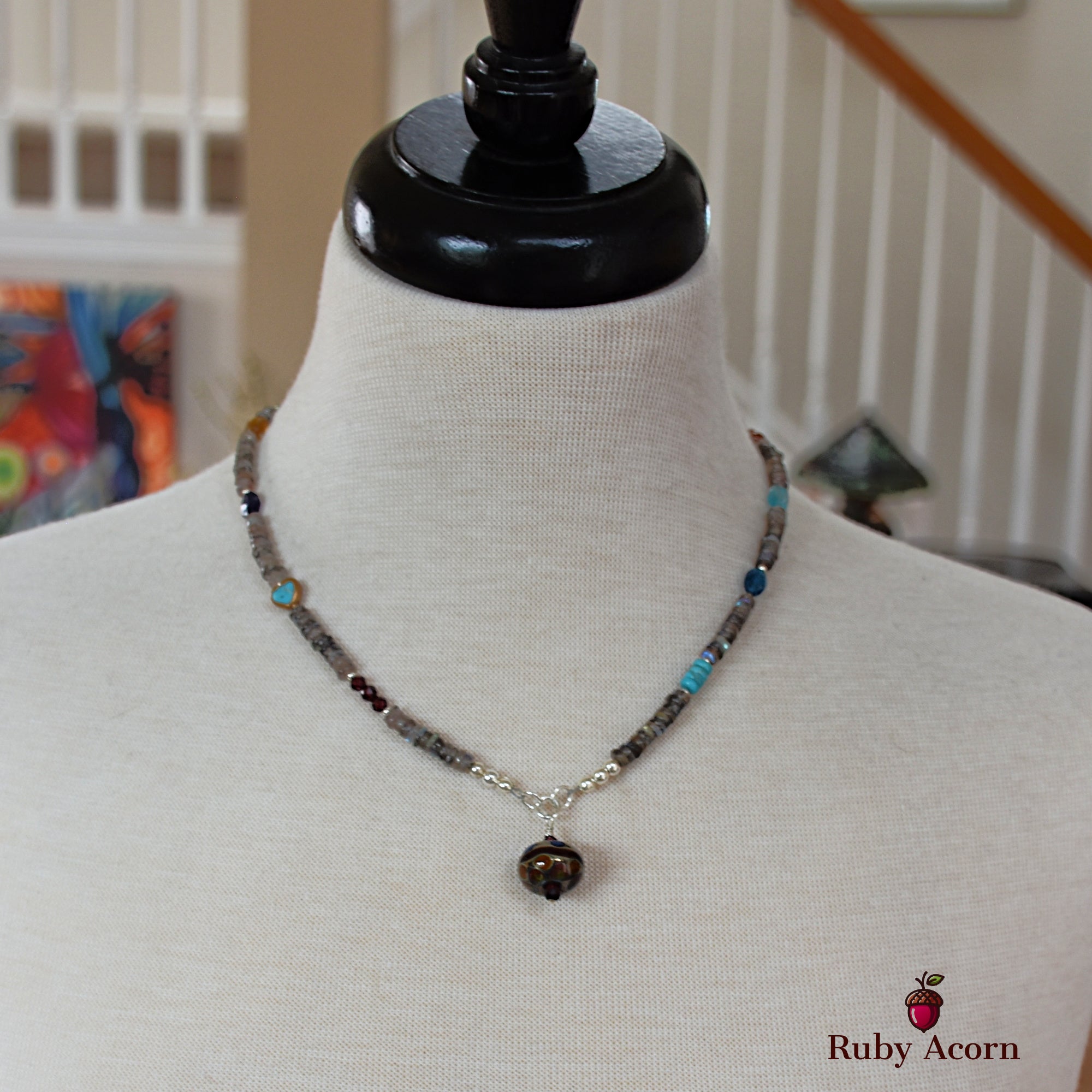 This image shows a necklace. It is displayed on a mannequin bust and features small beads with a pendant hanging in the center.