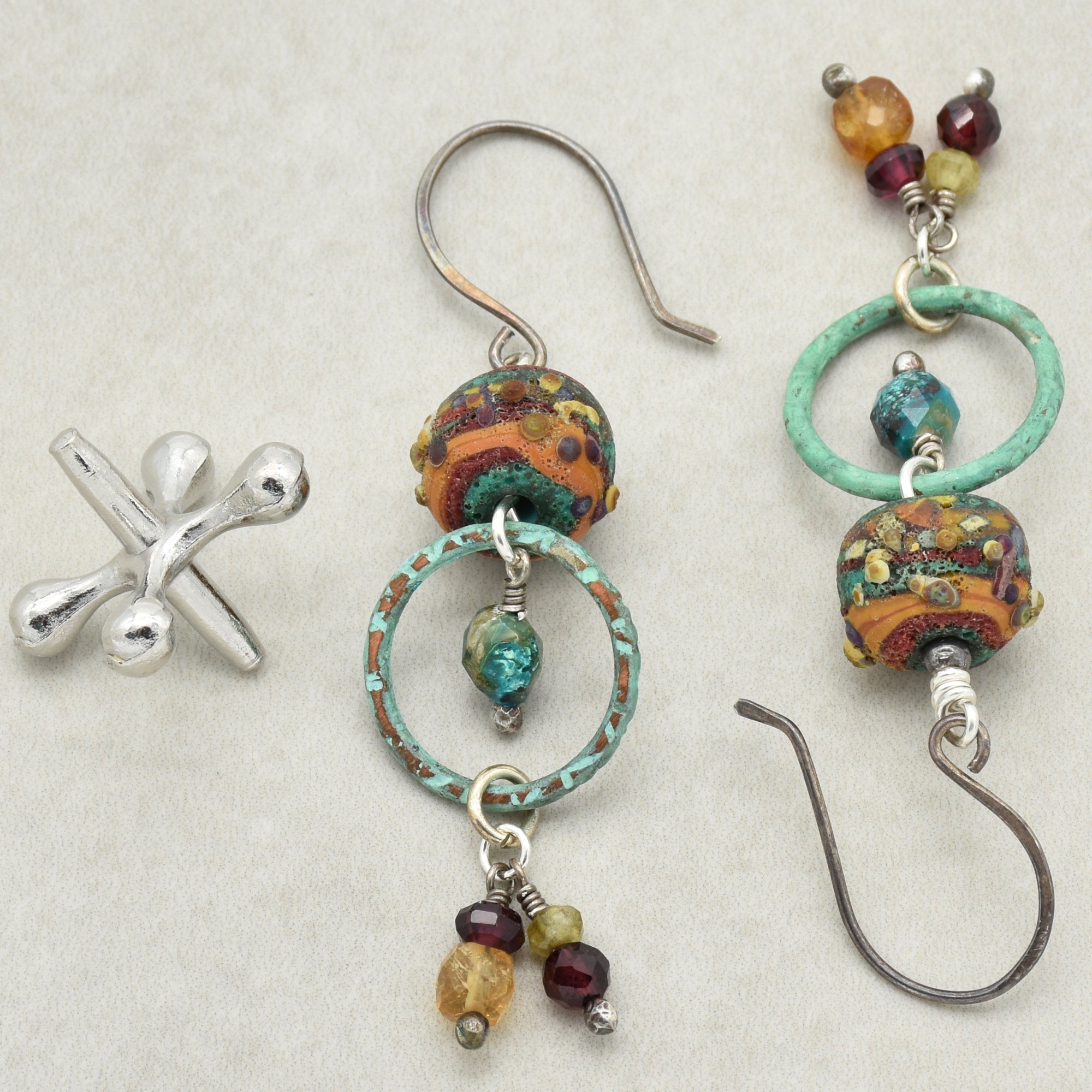 This image shows a pair of earrings. The items have hooks for piercing the ears, decorated with colorful beads and rings. There is also a separate silver piece that does not appear to be part of the earrings.