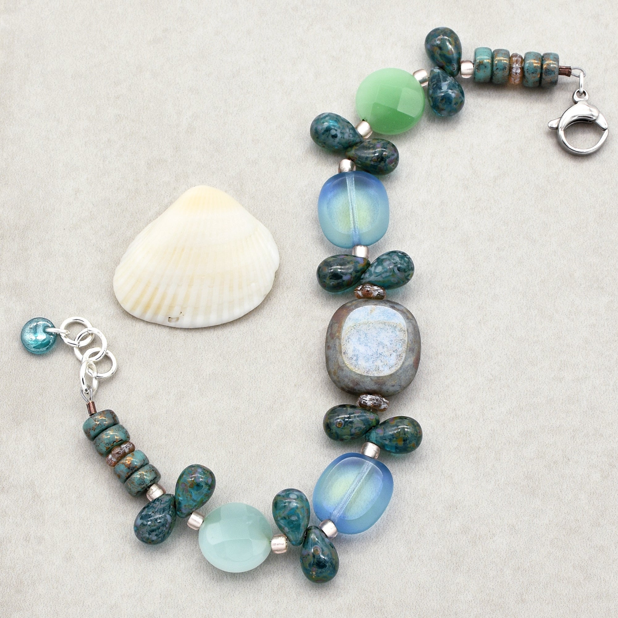 The jewelry in the image is a bracelet. It has a clasp fastening and is designed with various beads in shades of blue, green, and grey. The size and shape of the jewelry suggest it is meant to be worn around the wrist.