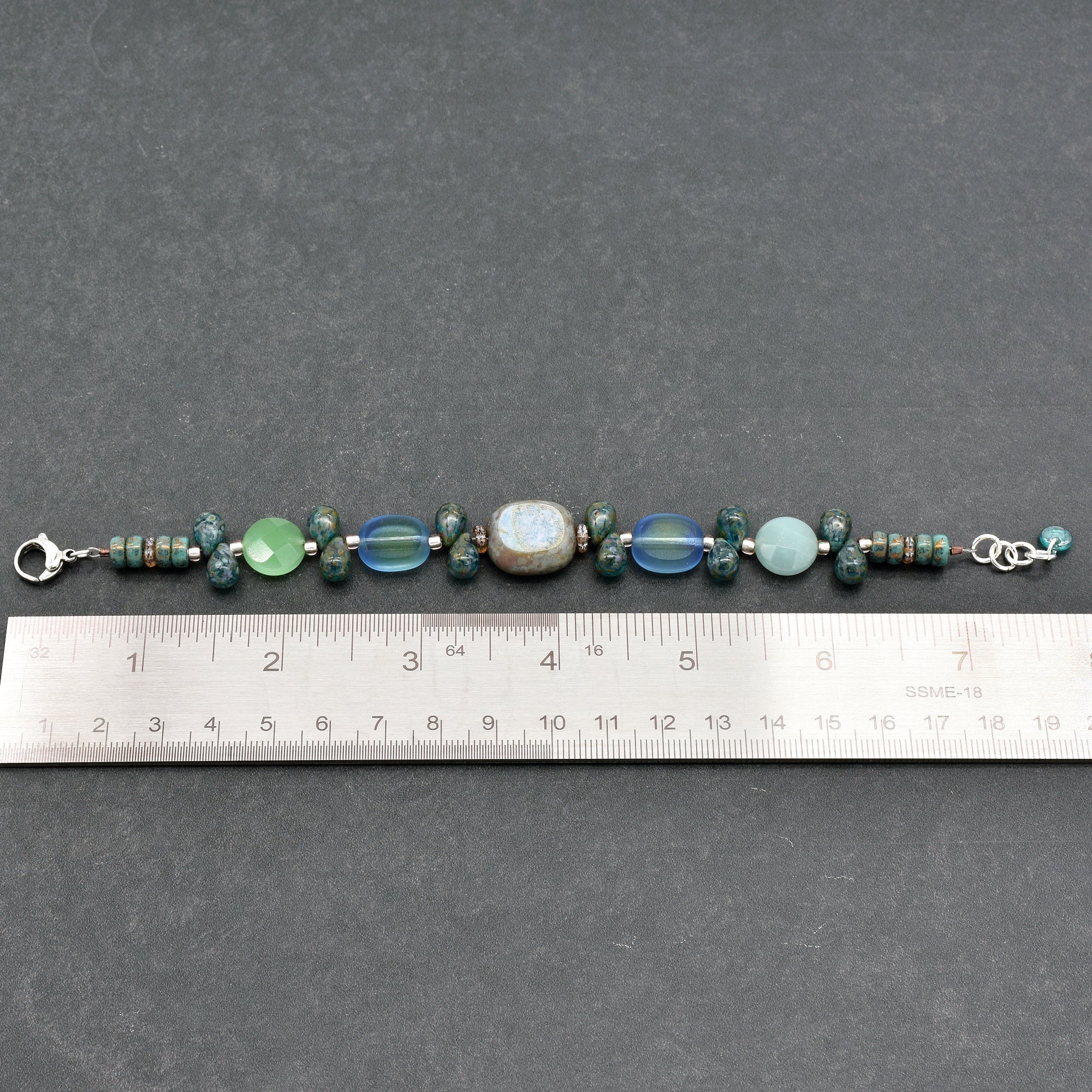 This image shows a bracelet. The length of the jewelry, as measured by the ruler below it, is approximately 7 inches, which is typical for a bracelet. Necklaces are usually longer, and earrings are typically smaller and designed to hang. The clasps on each end also indicate it is meant to be worn around the wrist.