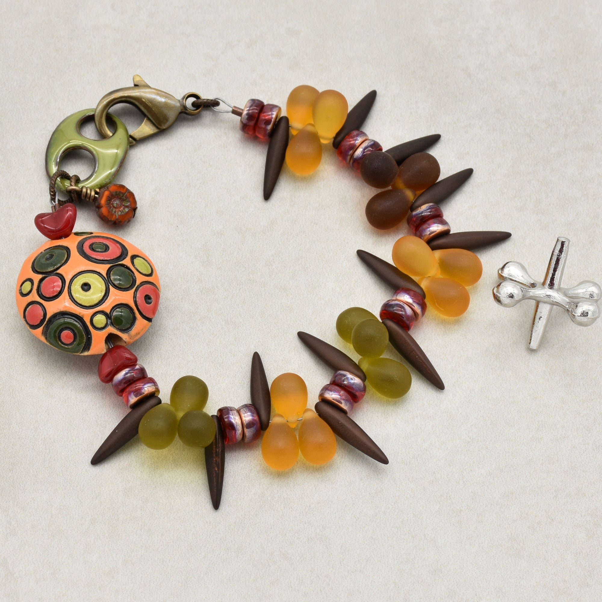 This image shows a bracelet. It has a clasp on one end and a toggle clasp on the other, which are typical for bracelets. The jewelry is decorated with various beads including teardrop-shaped beads, spikes, pancakes, and a decorative round piece with circular patterns.