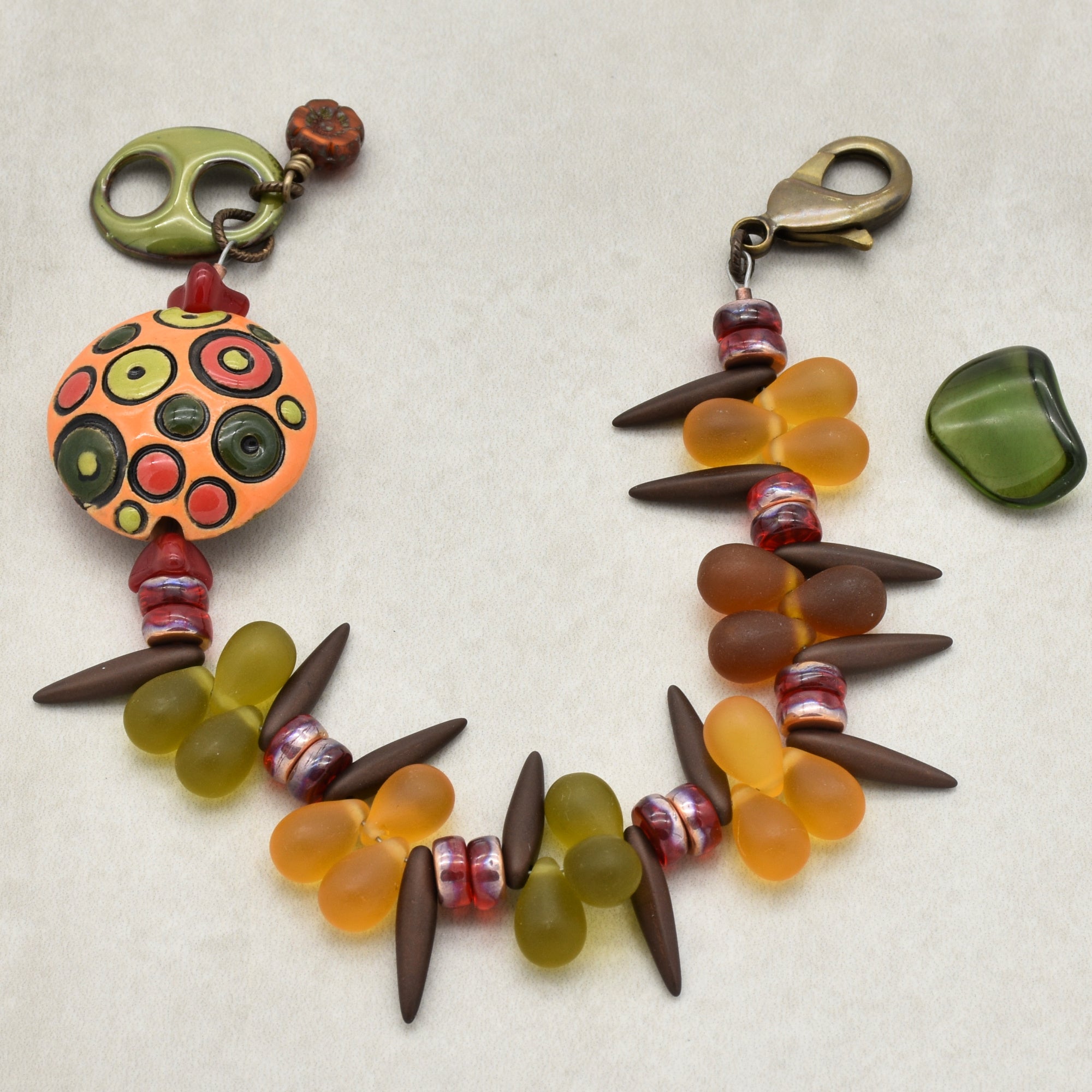 The jewelry item in the image is a bracelet. It features colorful beads in shades of green, orange, brown, and red, with a clasp for fastening.