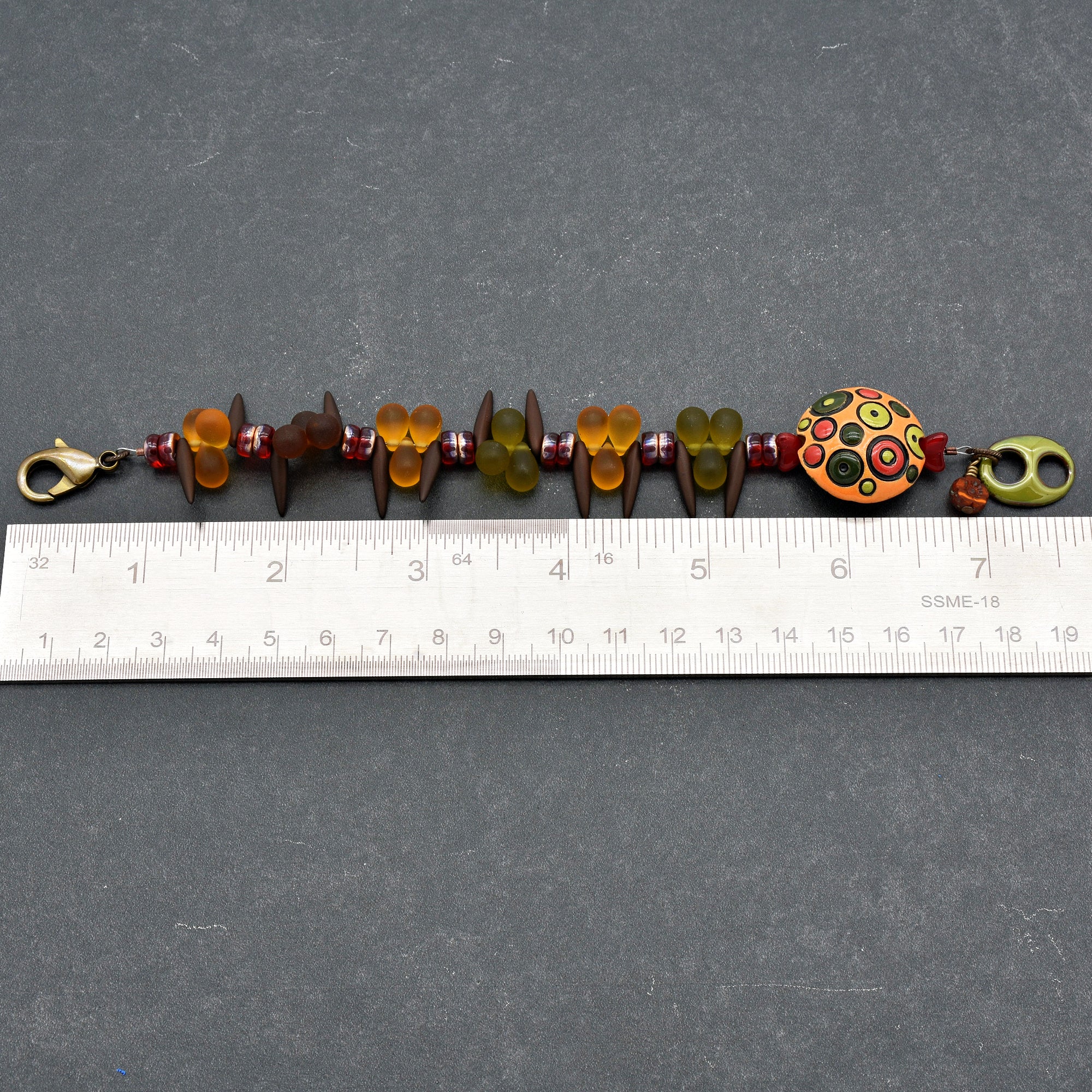 This image shows a bracelet. The jewelry piece is relatively short, as measured against the ruler below it, and it has a clasp that is typical for bracelets. The size and design are consistent with a bracelet rather than a necklace or an earring.