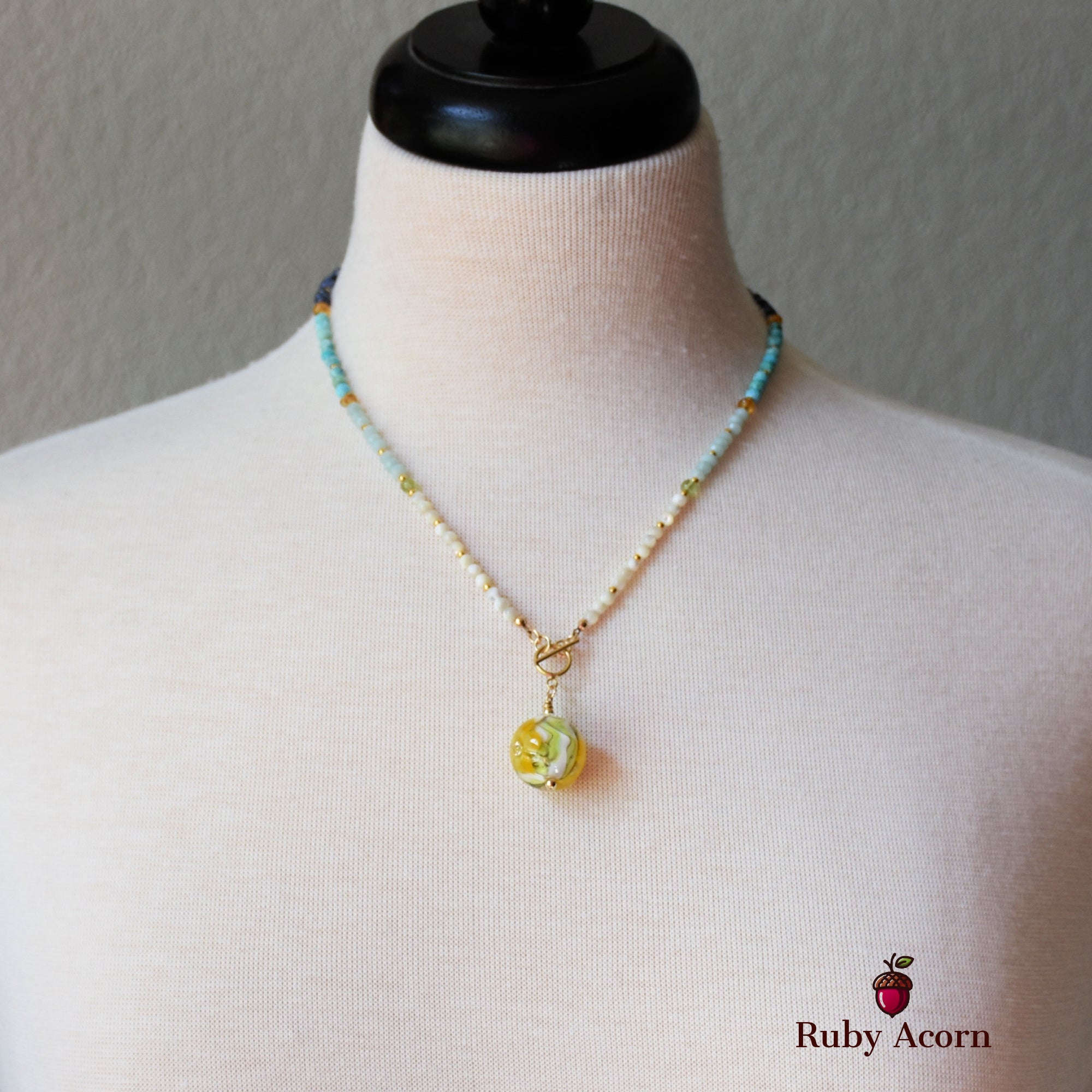The image shows a necklace made of small colorful beads with a round yellow pendant at the center.
