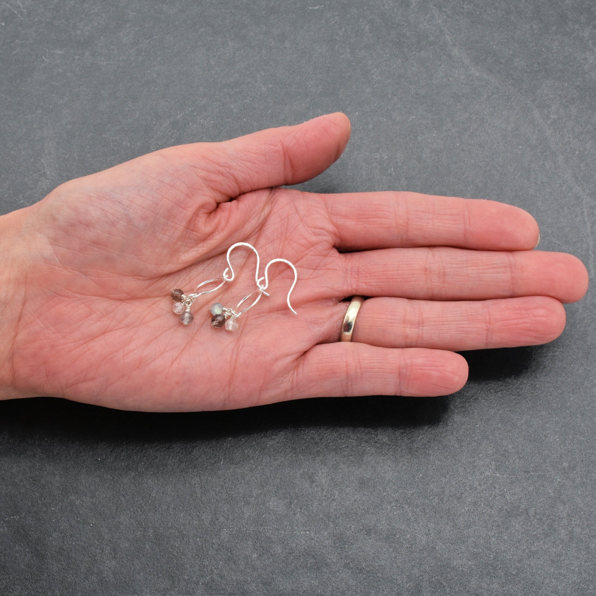 Hand holding two pairs of silver earrings against a gray background