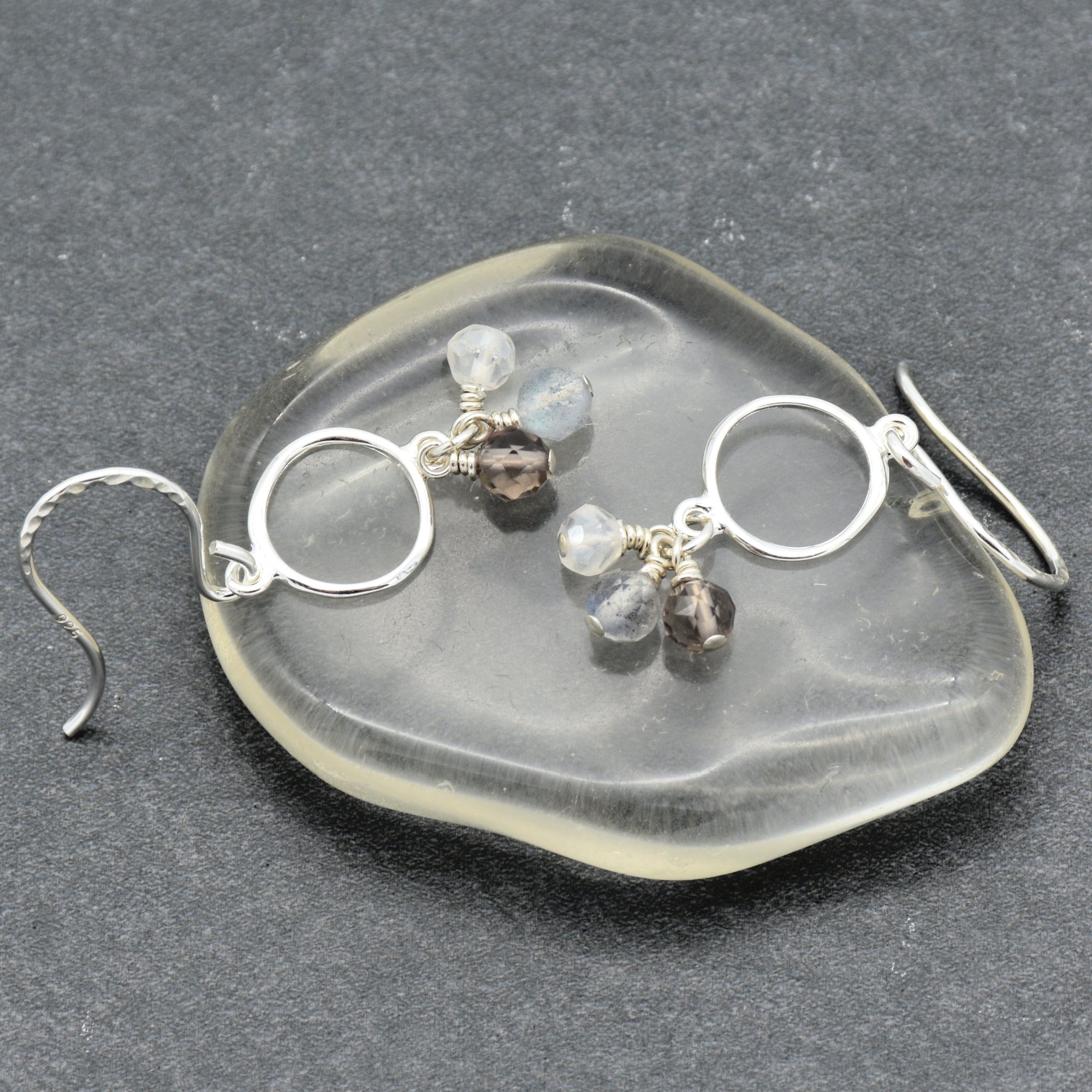 Silver earrings with gemstones on a clear stone surface