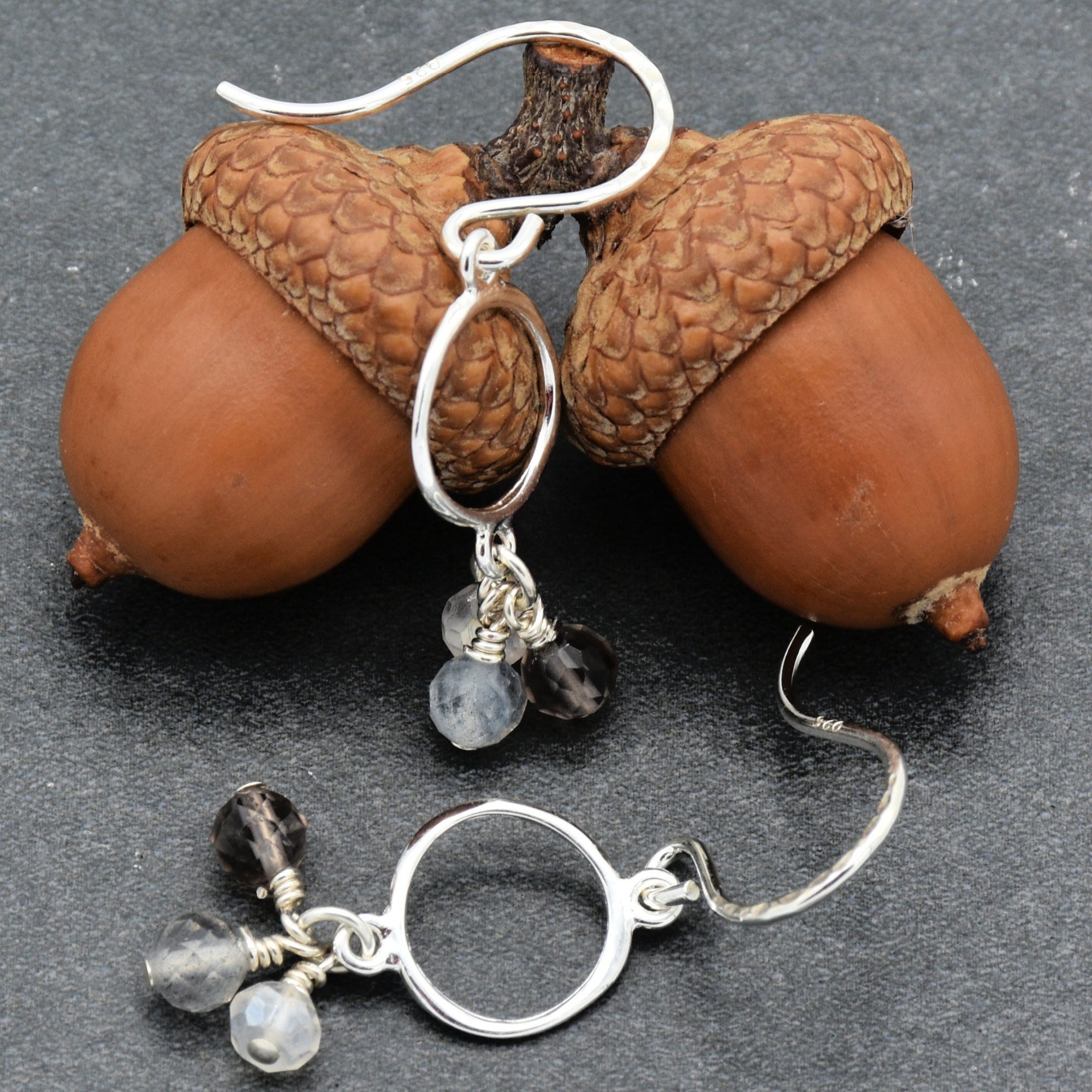 Silver earrings with gemstones on acorns against a dark background