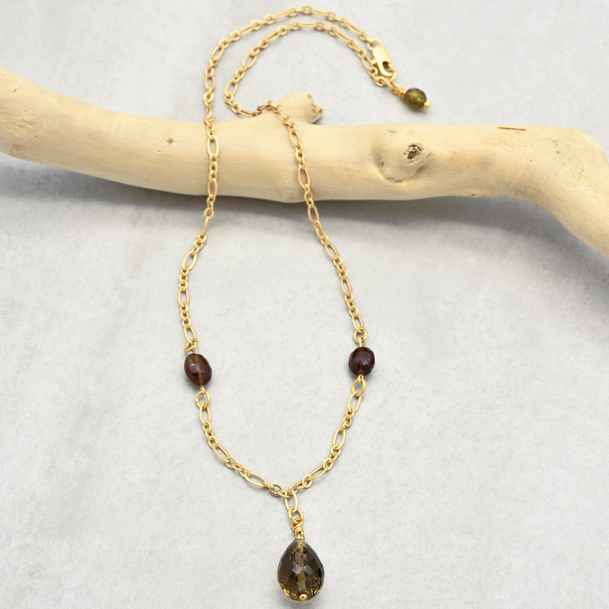 This image shows a necklace. It has a gold chain with decorative beads and a teardrop-shaped gemstone pendant hanging from it.