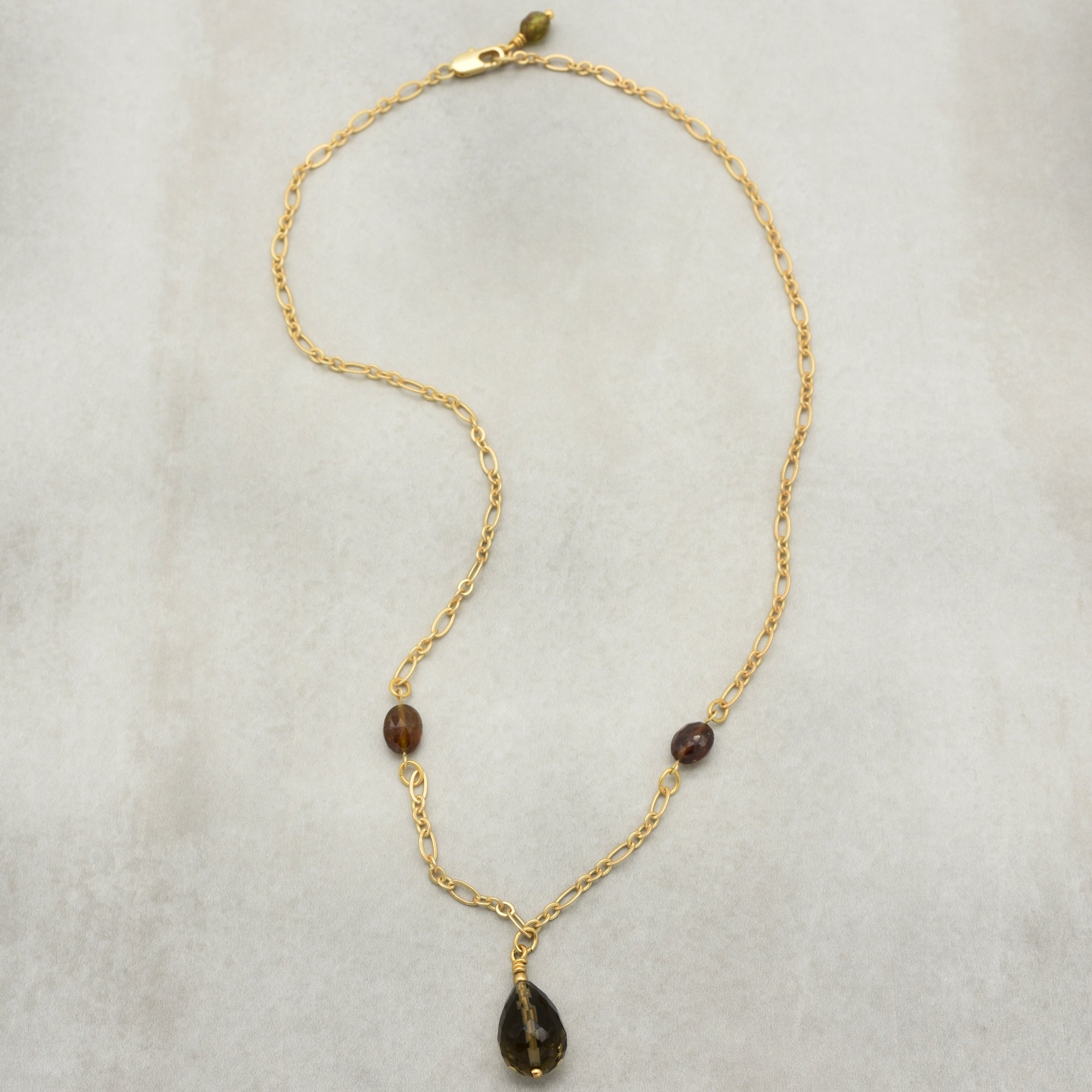 This image shows a necklace. It has a gold chain with two small beads and a teardrop-shaped pendant hanging in the center.