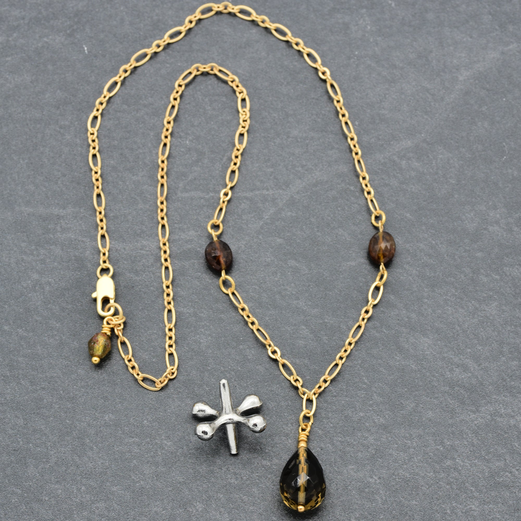 The image shows a necklace. It has a chain with a clasp, two dark beads on either side, and a teardrop-shaped pendant hanging from the center.