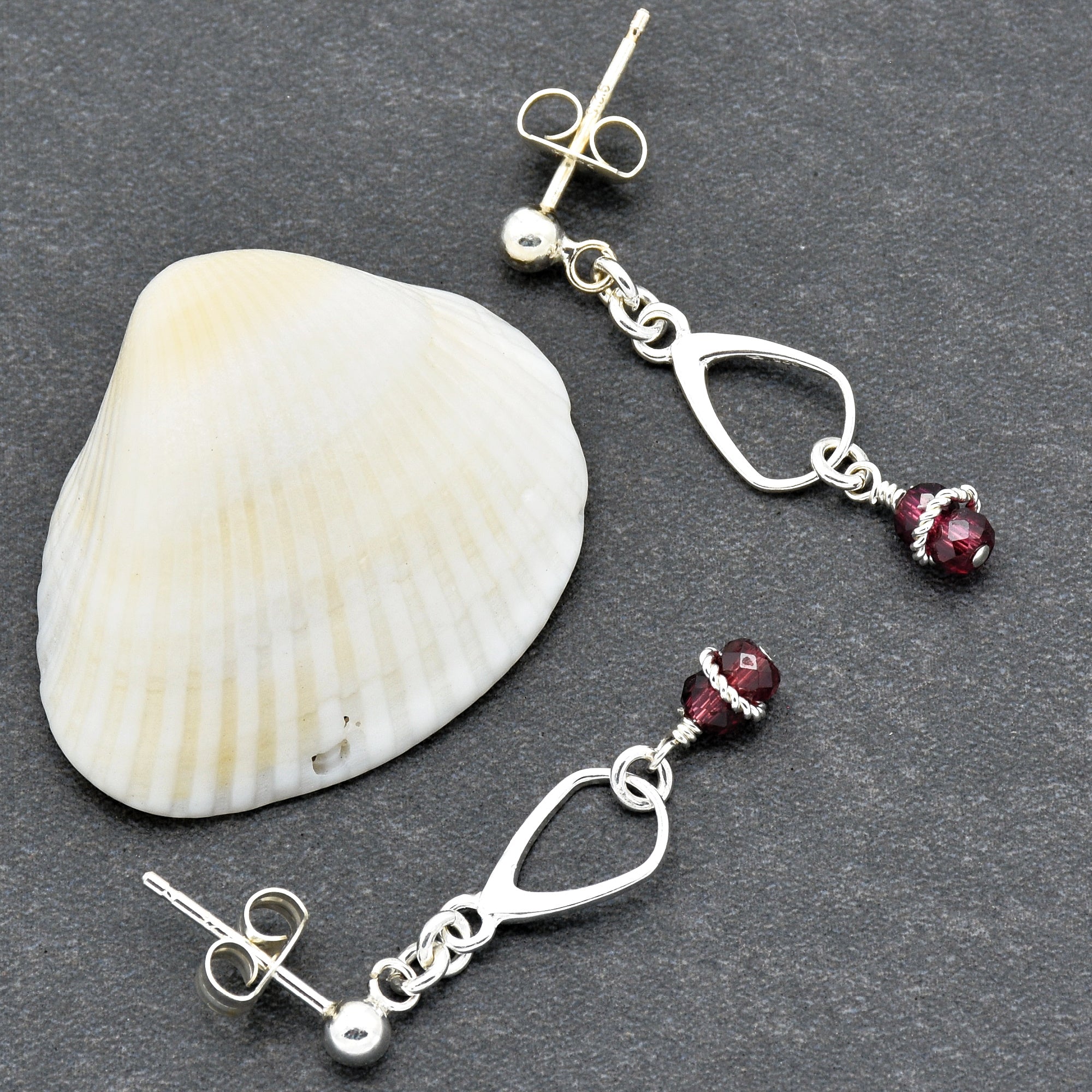 This image shows a pair of earrings. They are designed with a silver post and a dangling element that includes a silver geometric shape and a small purple bead.