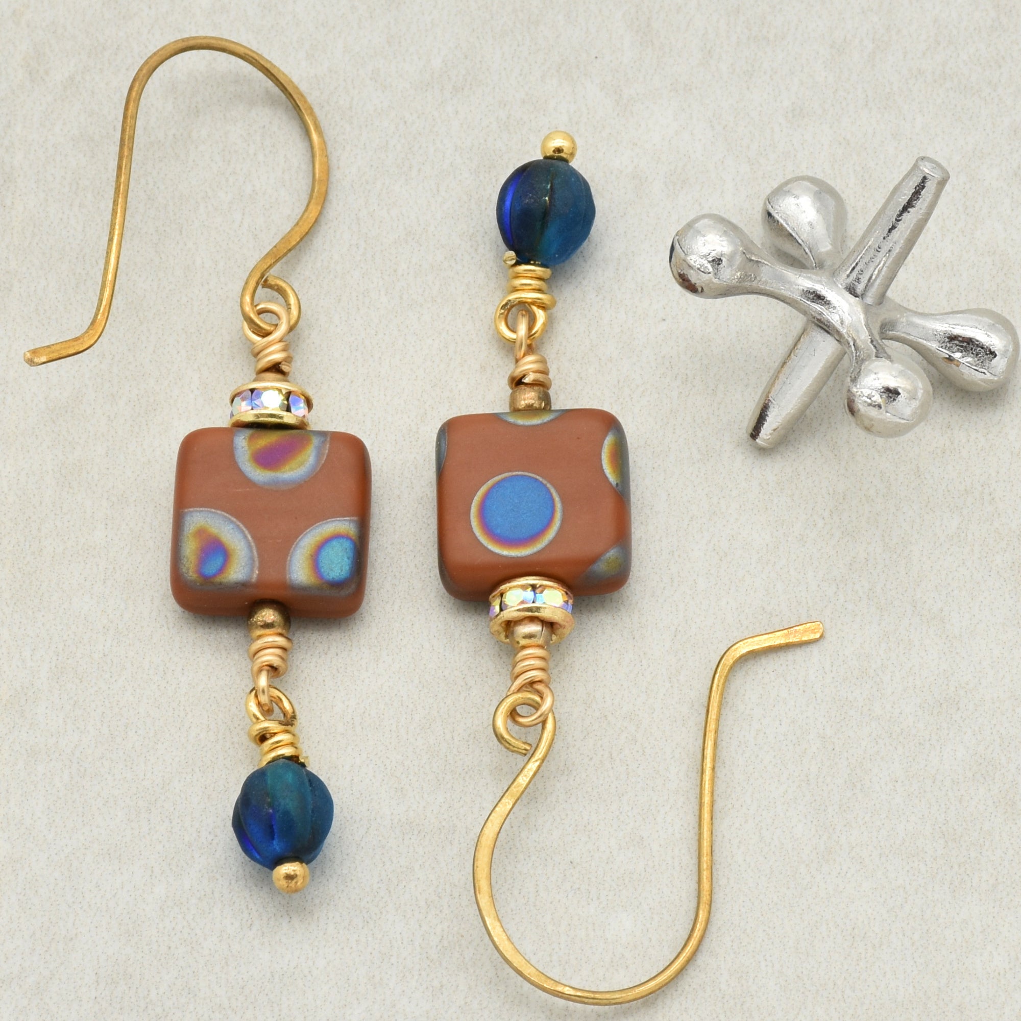 The image shows a pair of earrings. The pieces have hooks that go through pierced ears and decorative beads. There is also a silver jacks game piece visible in the image, but the jewelry items themselves are clearly earrings.