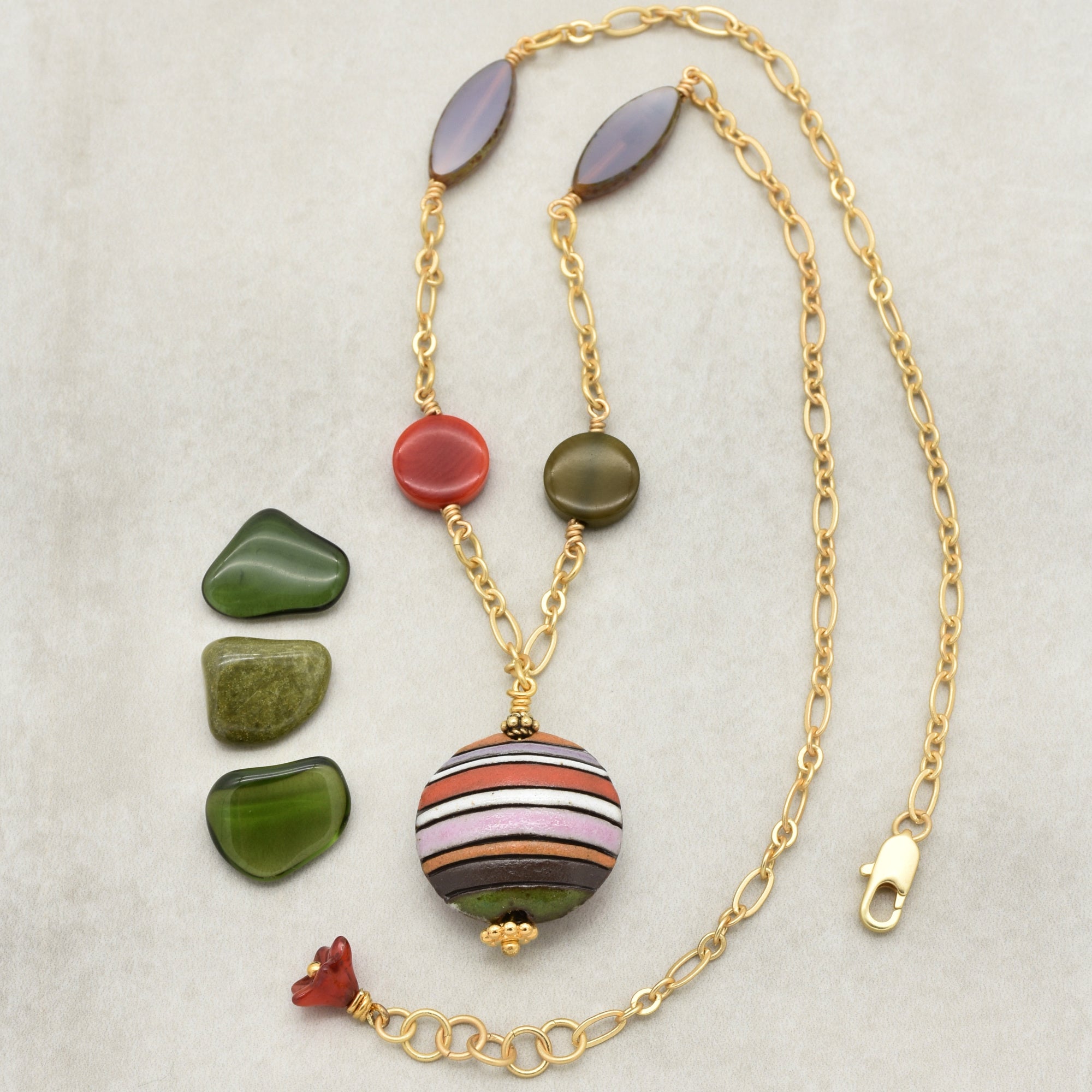 This image shows a necklace. It has a gold chain with various beads, including a large, round, striped bead as a pendant, and several other smaller beads along the chain. The lobster clasp closure at the end confirms it is likely a necklace rather than an earring or bracelet.