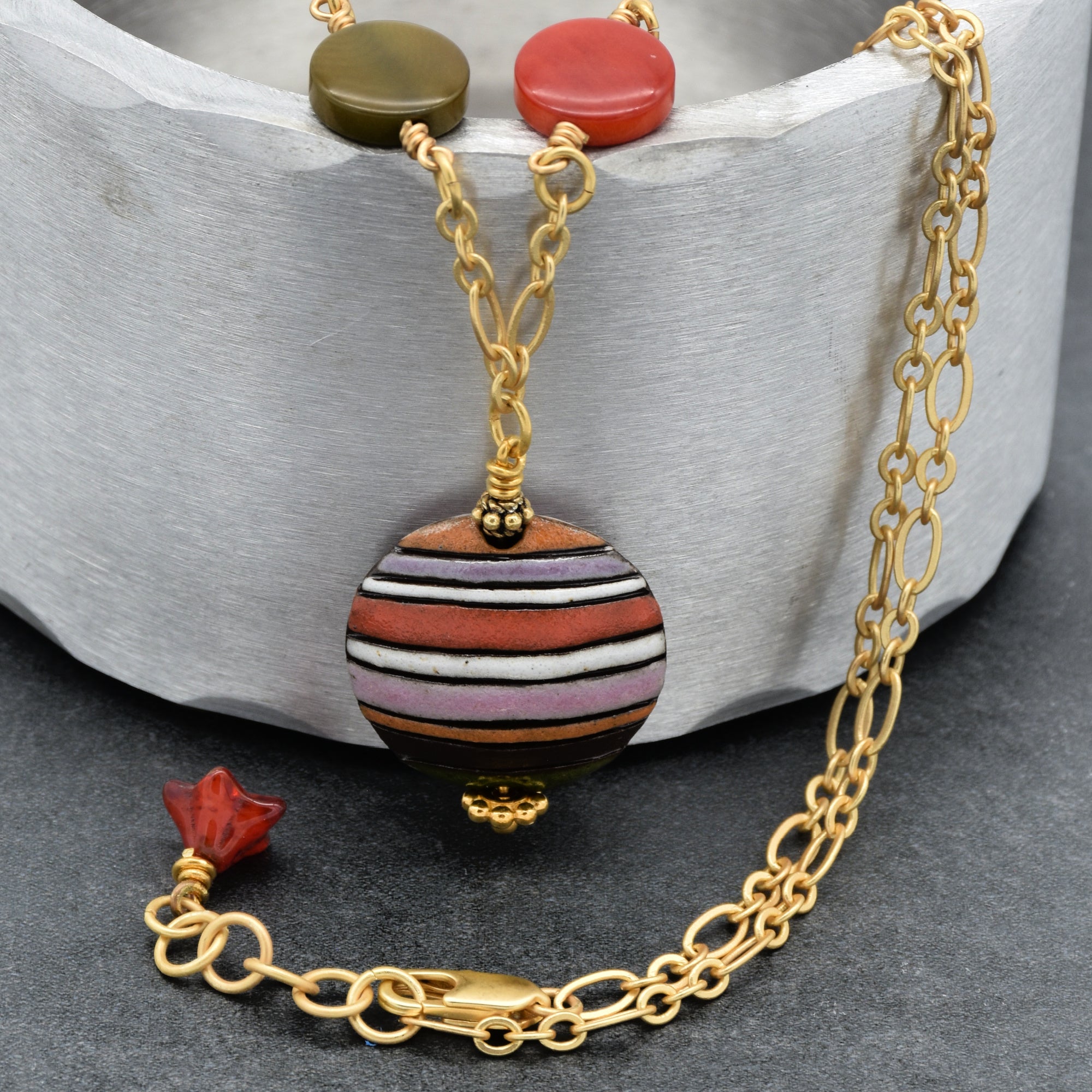This image shows a necklace. The jewelry features a gold chain with a central striped bead pendant and some additional decorative beads near the clasp.