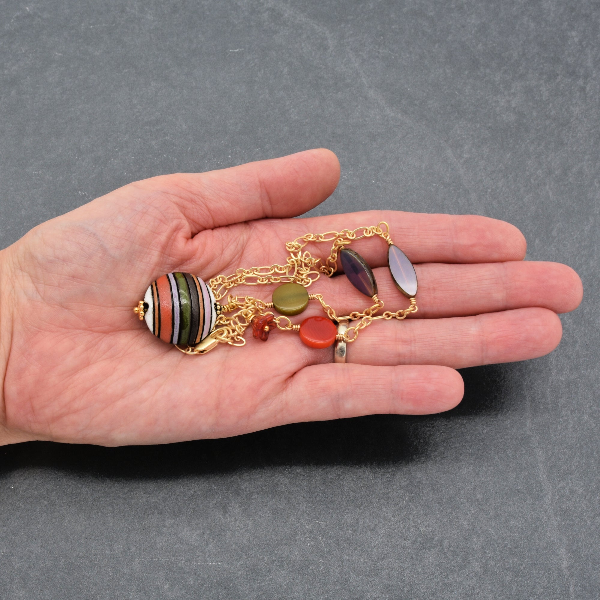 This image shows a bracelet. The jewelry piece is relatively short in length, has a chain with various beads, and is being held in a person's hand, which highlights its size as suitable for a bracelet.