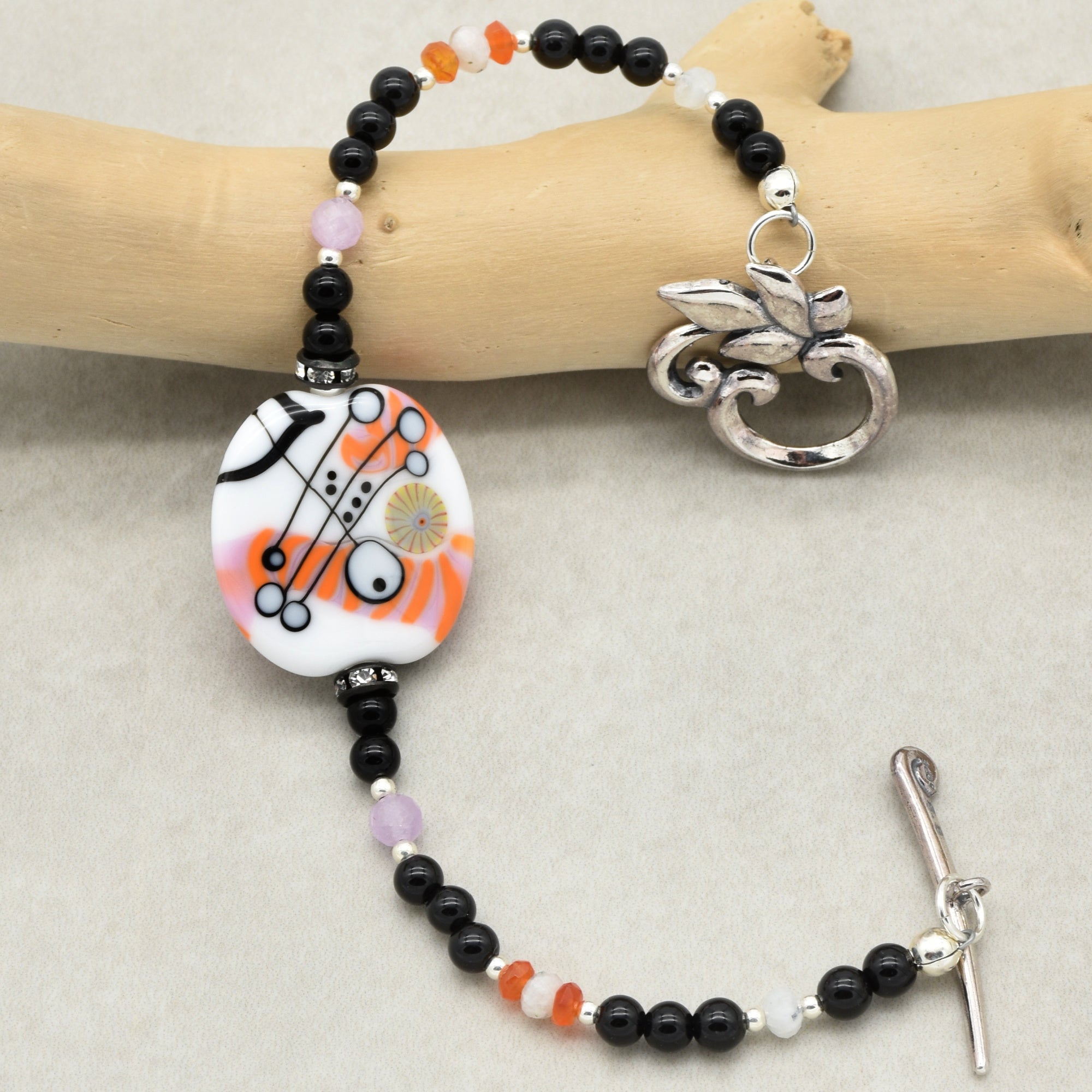 This image shows a bracelet. The size and the presence of a toggle clasp, as well as the way it is laid out, indicate it is meant to be worn around the wrist. The beading and central large decorative bead also fit the typical design of a bracelet rather than a necklace or earring.