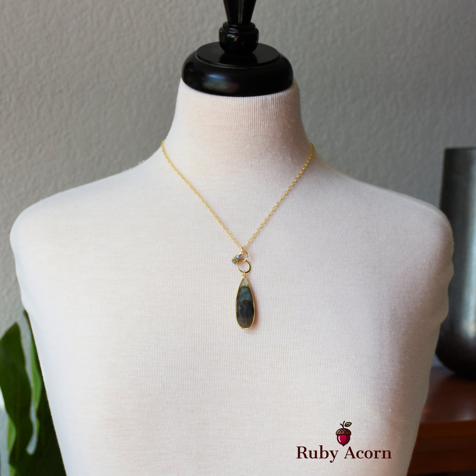 This image shows a necklace displayed on a mannequin. The necklace has a delicate gold chain with a teardrop-shaped pendant.