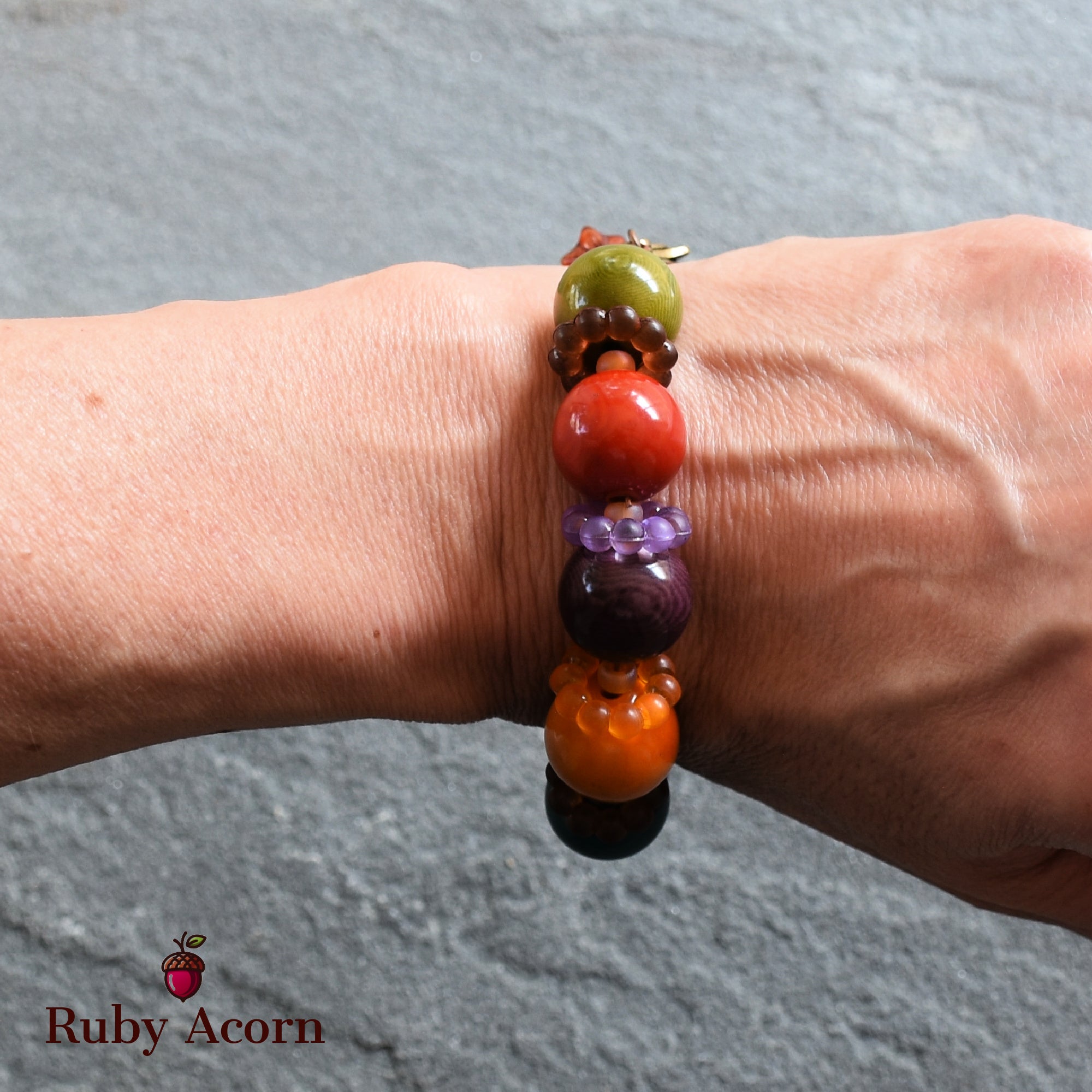The image shows a bracelet. It is worn around the wrist and features large, colorful beads in various shades such as green, red, purple, and orange.