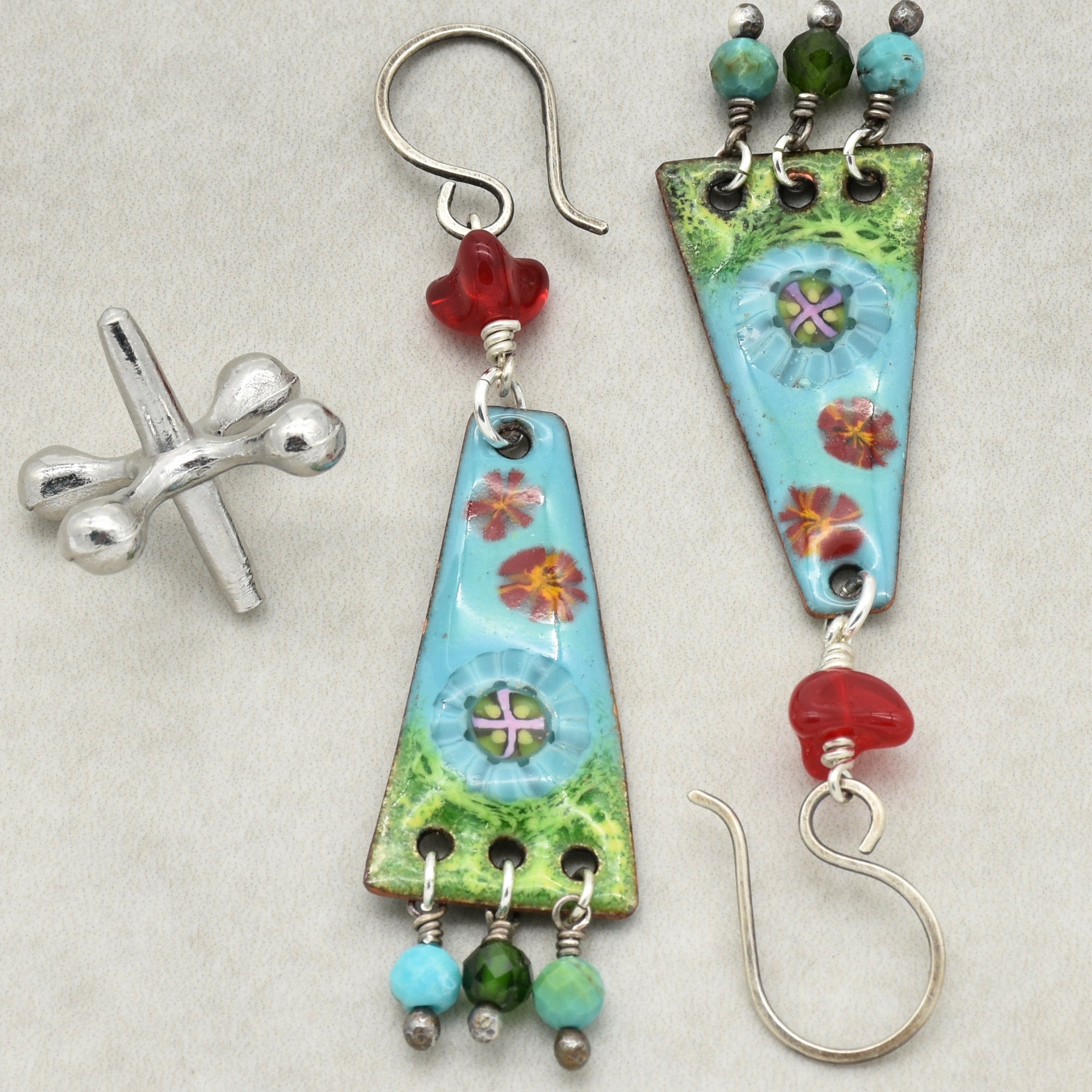 The image shows a pair of earrings. The earrings have a hook for piercing, which identifies them as earrings rather than a necklace or bracelet. They feature a triangular design with colorful beads and floral patterns.