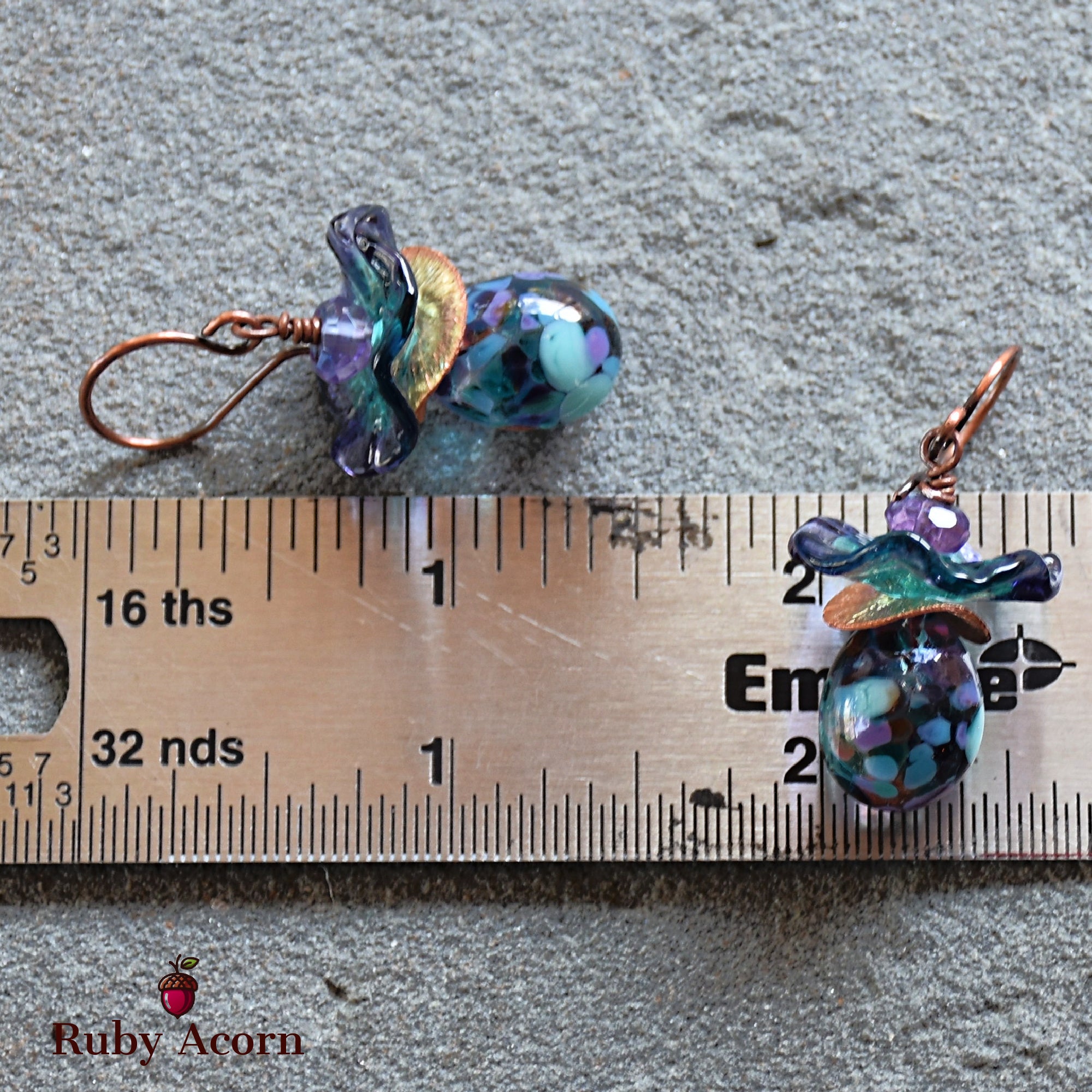 This image shows a pair of earrings. The jewelry pieces have hooks typical of earrings and are placed next to a ruler for size reference.