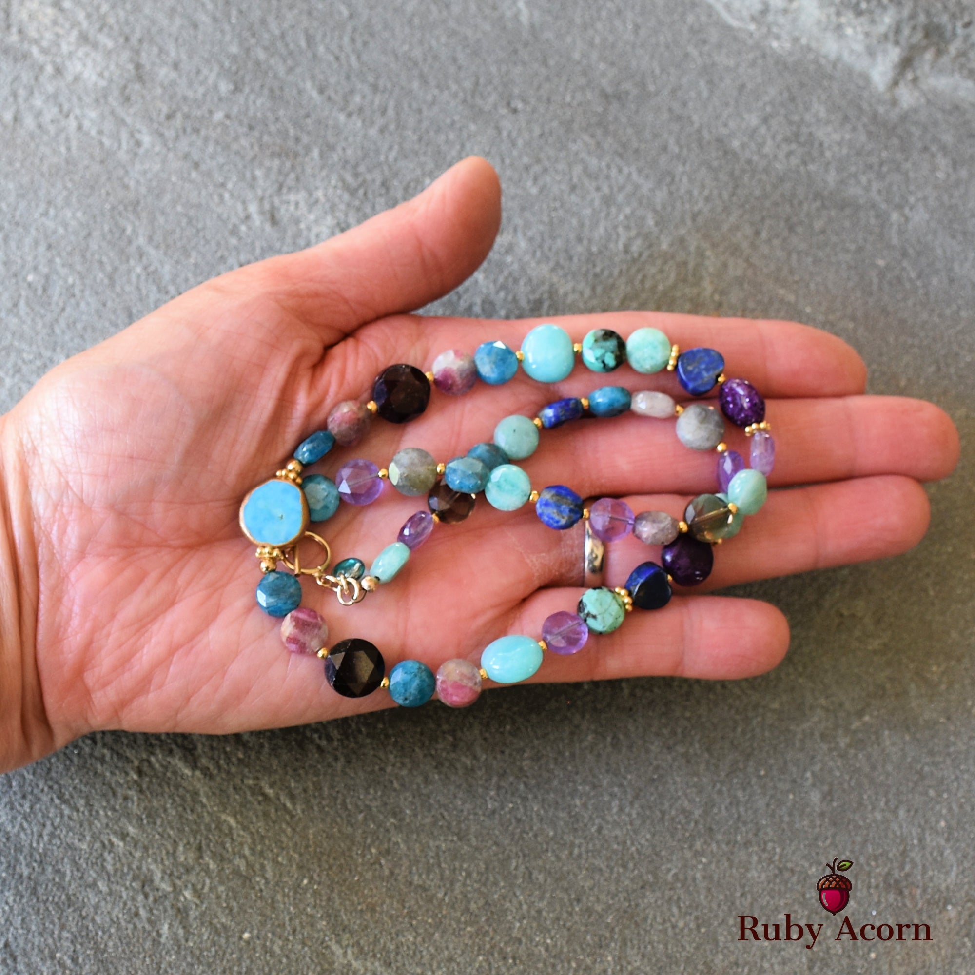 This image shows a beaded necklace. The jewelry features various colorful beads strung together, and the necklace clasp is visible near the thumb, indicating it is designed to be worn around the neck.