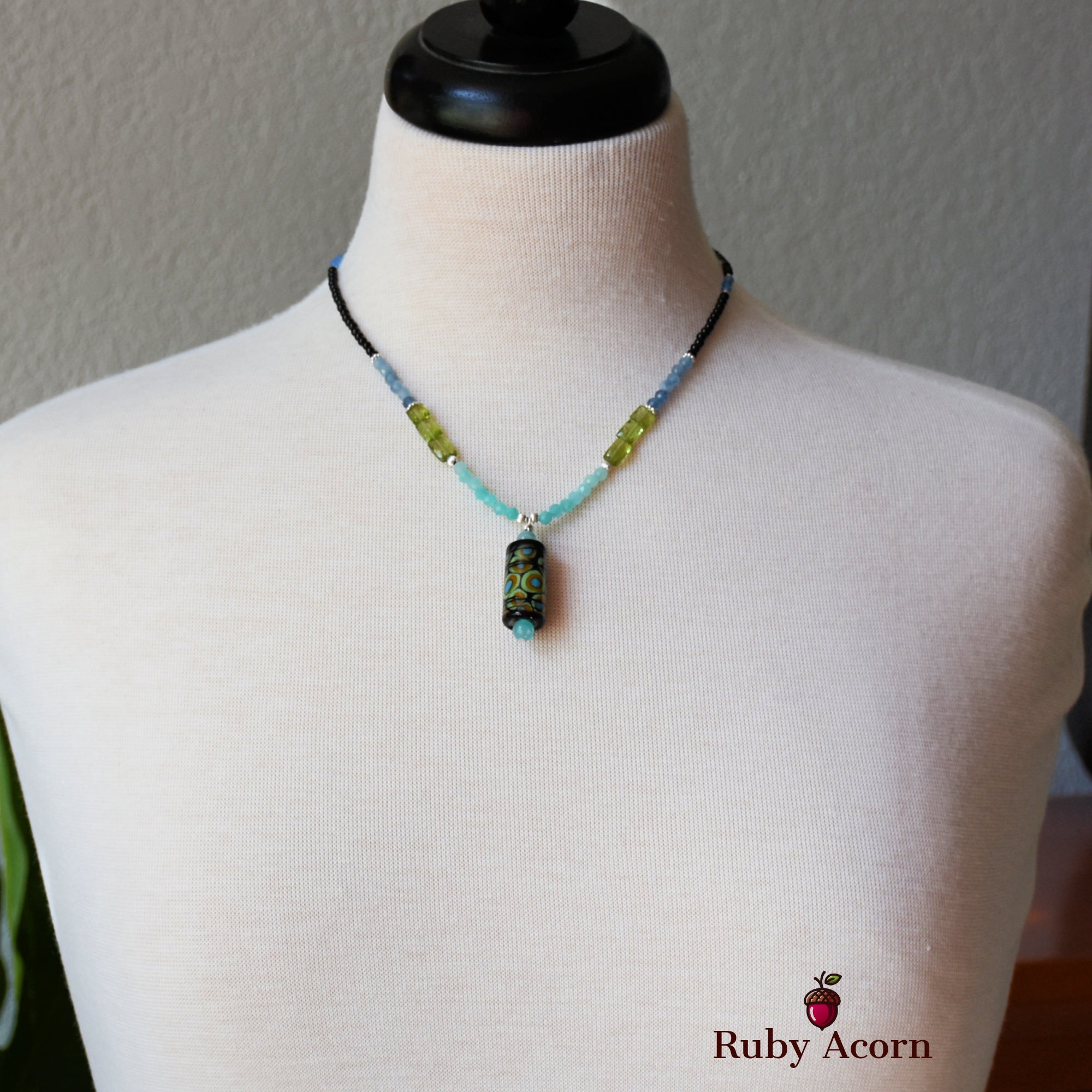 This image shows a necklace. It is displayed on a mannequin and features a beaded design with a pendant in the center.