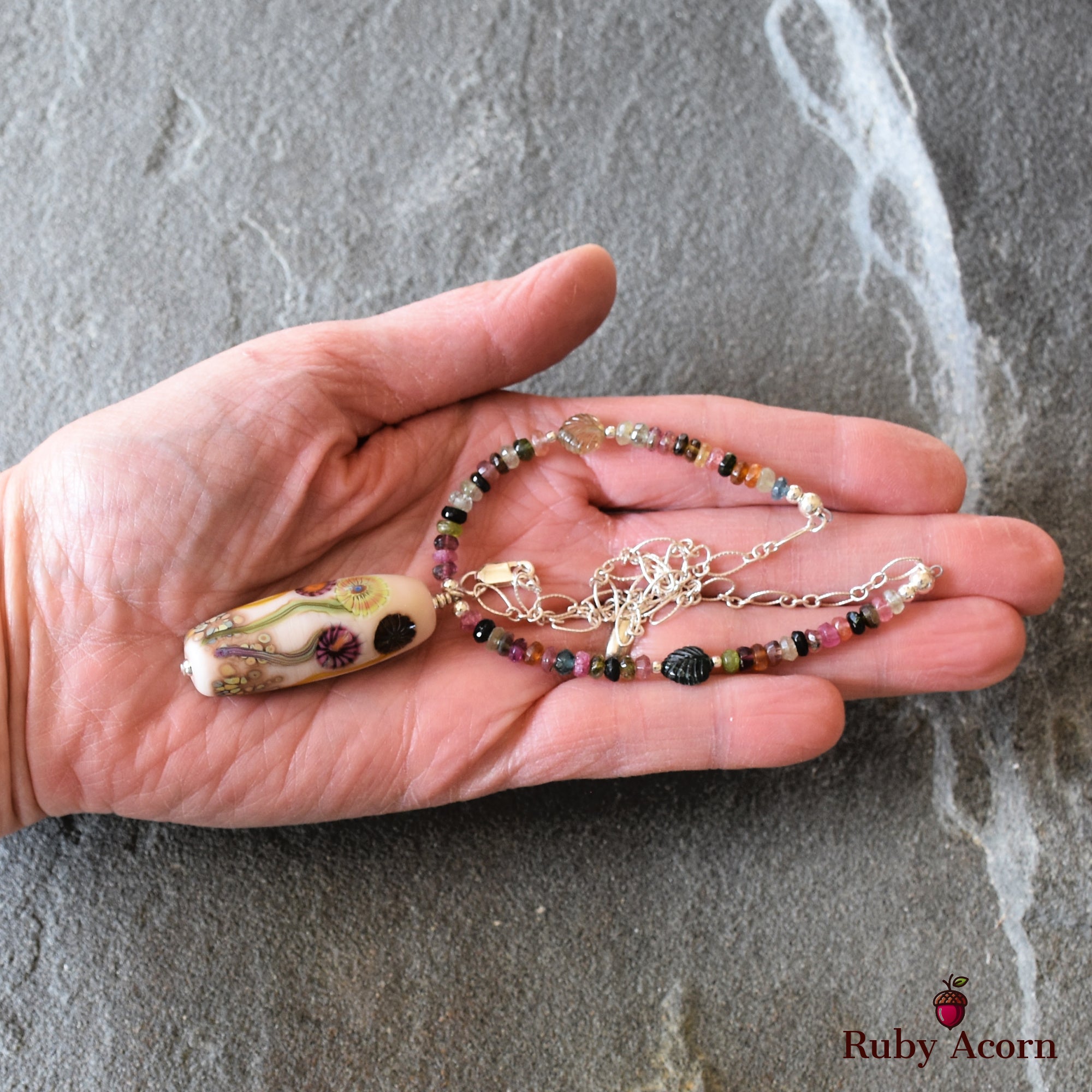 This image shows a necklace. The jewelry consists of a pendant with colorful floral designs and a chain made of small multicolored beads.