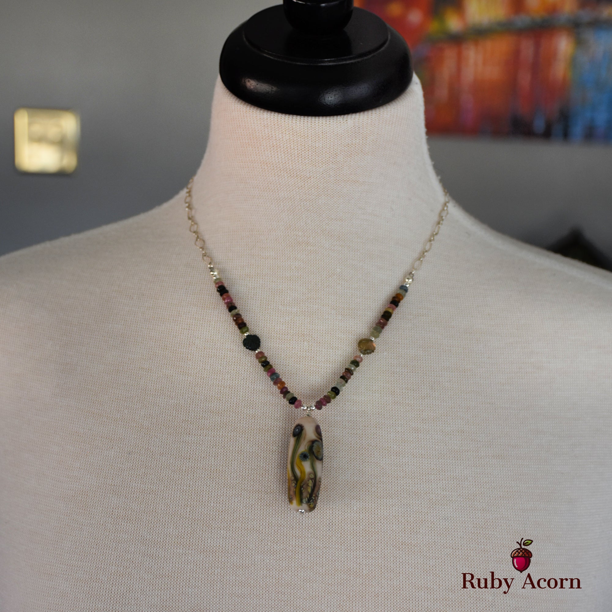 This image shows a necklace. It features a pendant with a multicolored beaded chain displayed on a mannequin.