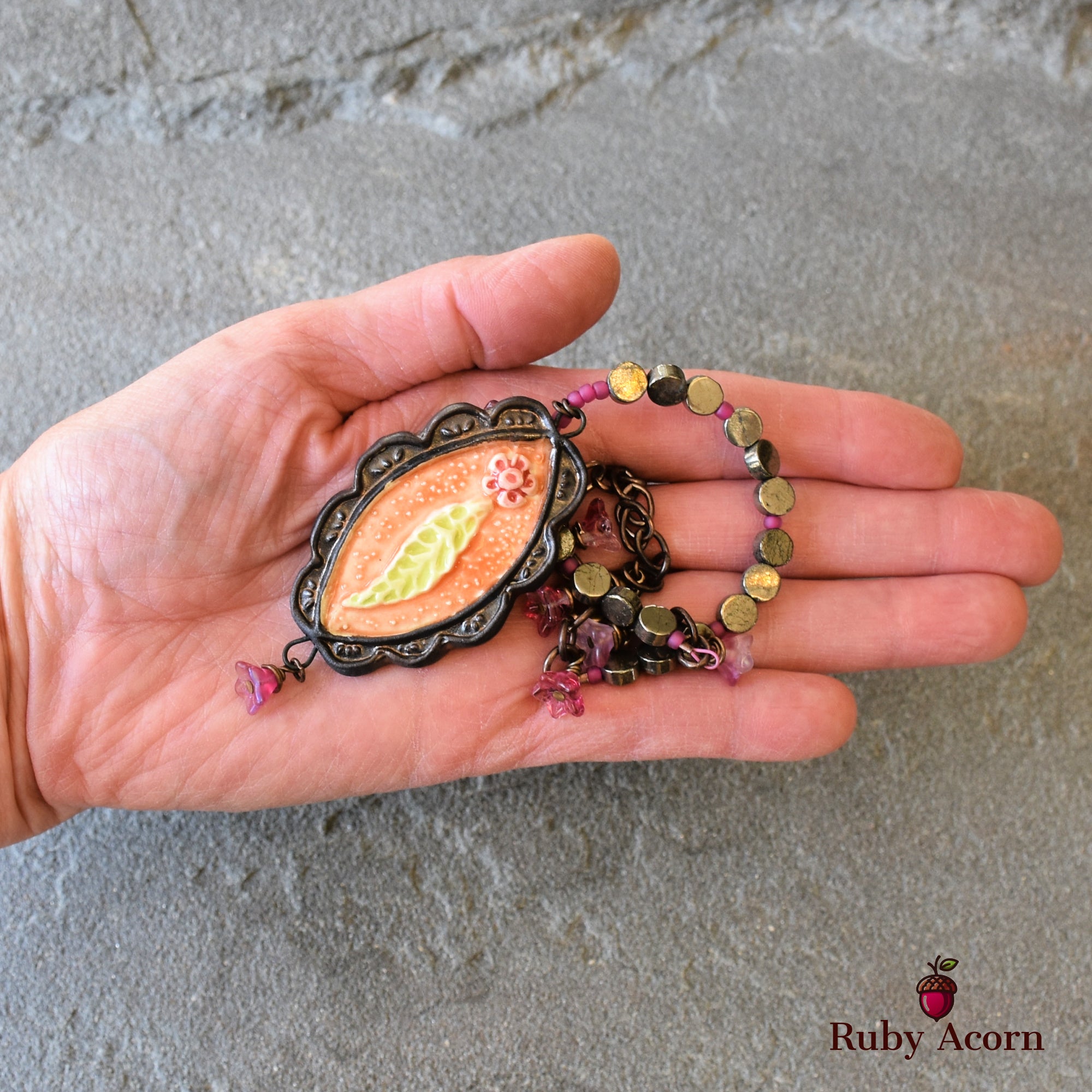 This image shows a necklace. The piece of jewelry has a decorative pendant with a leaf and flower design and beads attached to a chain, indicating it is meant to be worn around the neck.