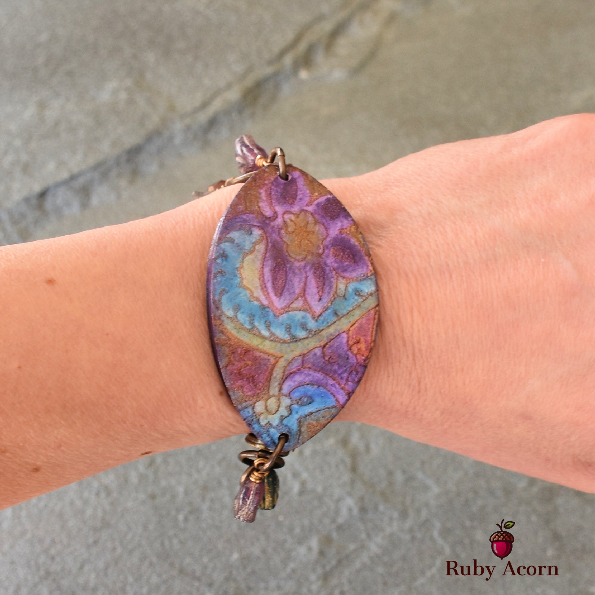 The jewelry in the image is a bracelet. It is shown wrapped around a wrist and has a large, colorful, oval-shaped decorative piece with a floral design.