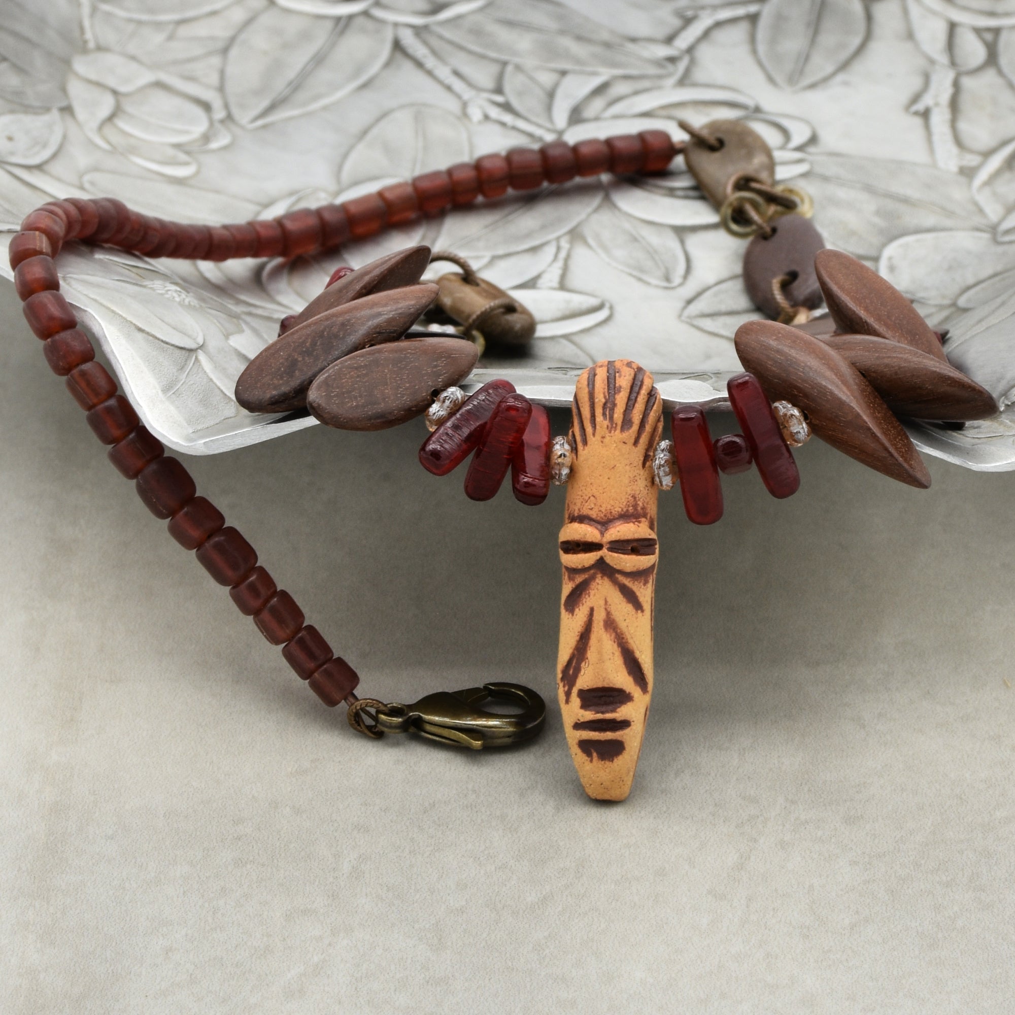 This image shows a bracelet. It has a clasp, various beads including a carved central piece that resembles a mask or face, and the overall size and structure are consistent with a bracelet rather than a necklace or earring.