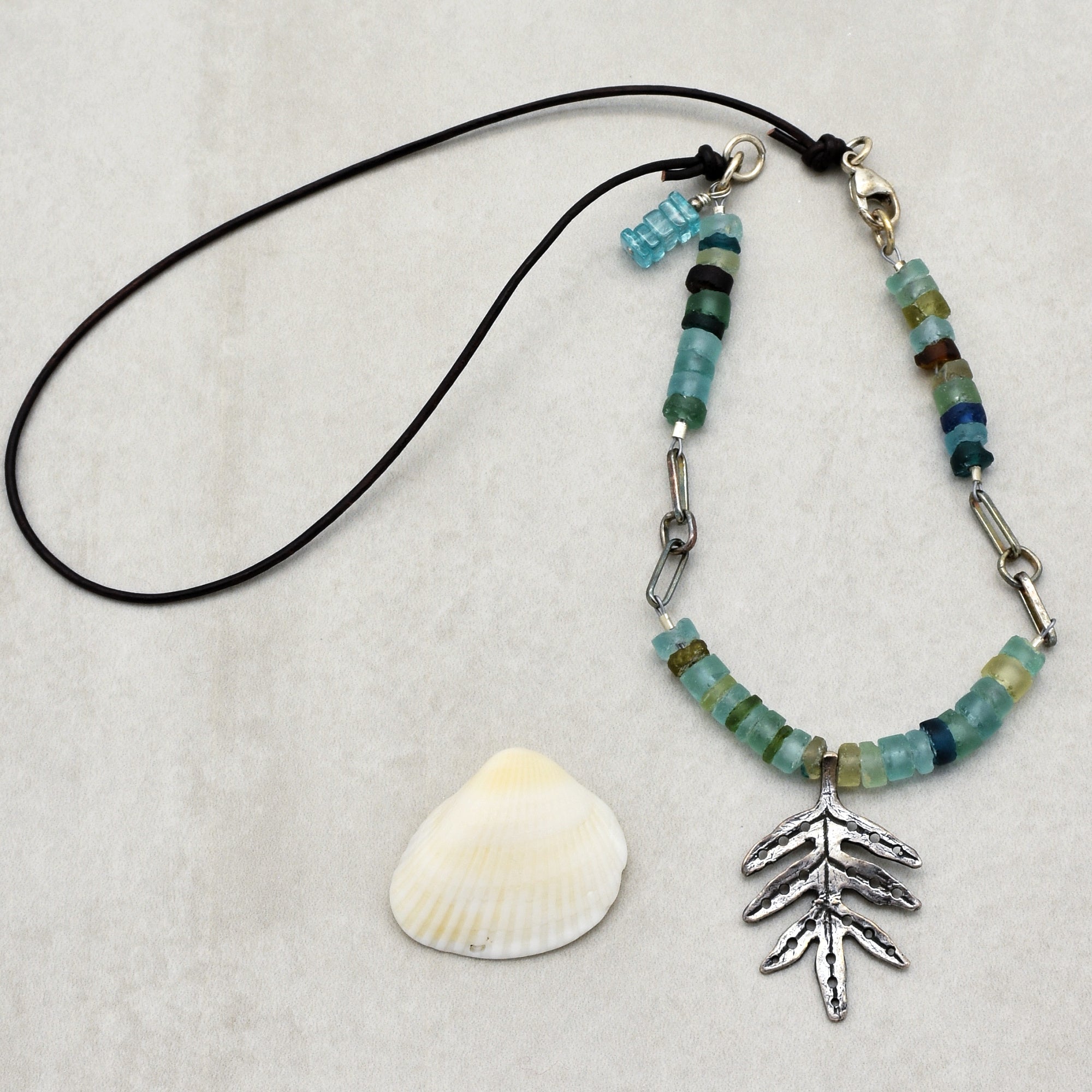 This image shows a bracelet. It has a string with beads and a metallic leaf-shaped charm attached, along with a lobster clasp for fastening around the wrist.