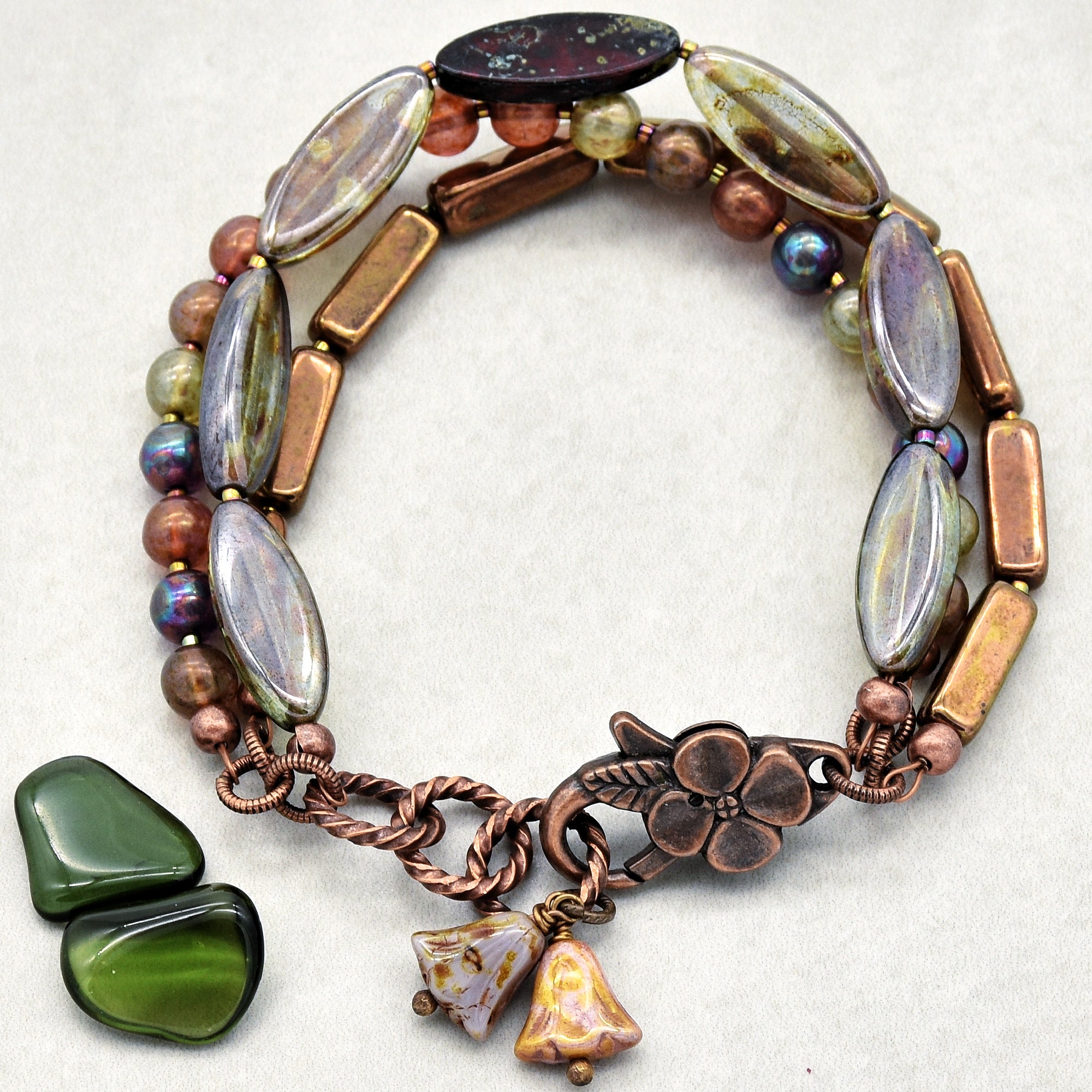 The jewelry in the image is a bracelet. It is composed of multiple strands of beads, including metallic and glass-like pieces, and has a floral-themed clasp with small flower charms attached.