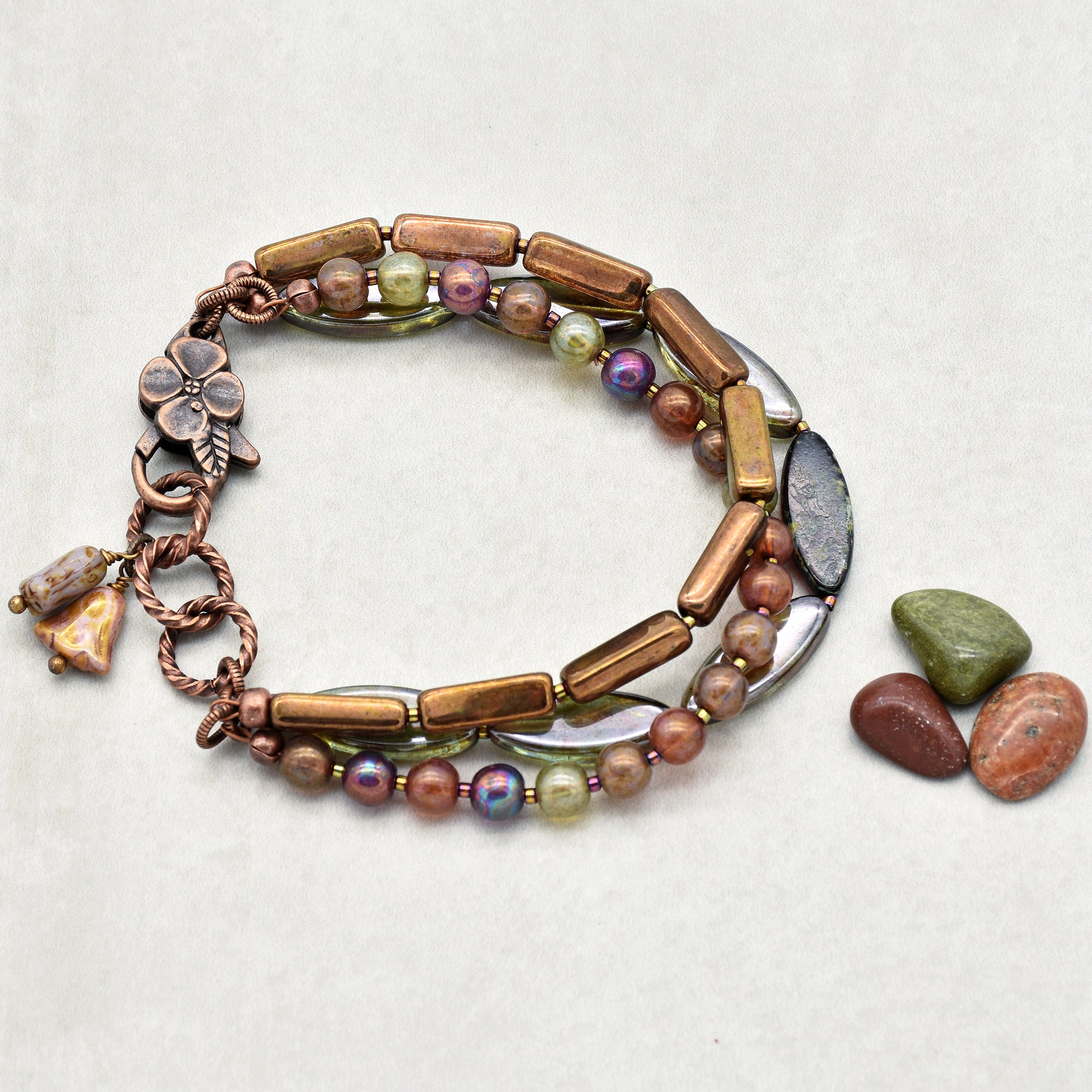 This image shows a bracelet. It consists of multiple strands of beads in various colors and shapes, including round and rectangular beads, with a clasp featuring a flower design. The size and style indicate that it is meant to be worn around the wrist.