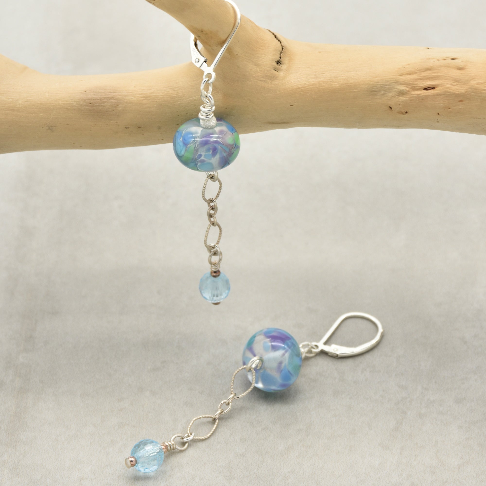 This image shows a pair of earrings. They have a hook at the top for attaching to the ear and feature decorative beads and chains hanging down.