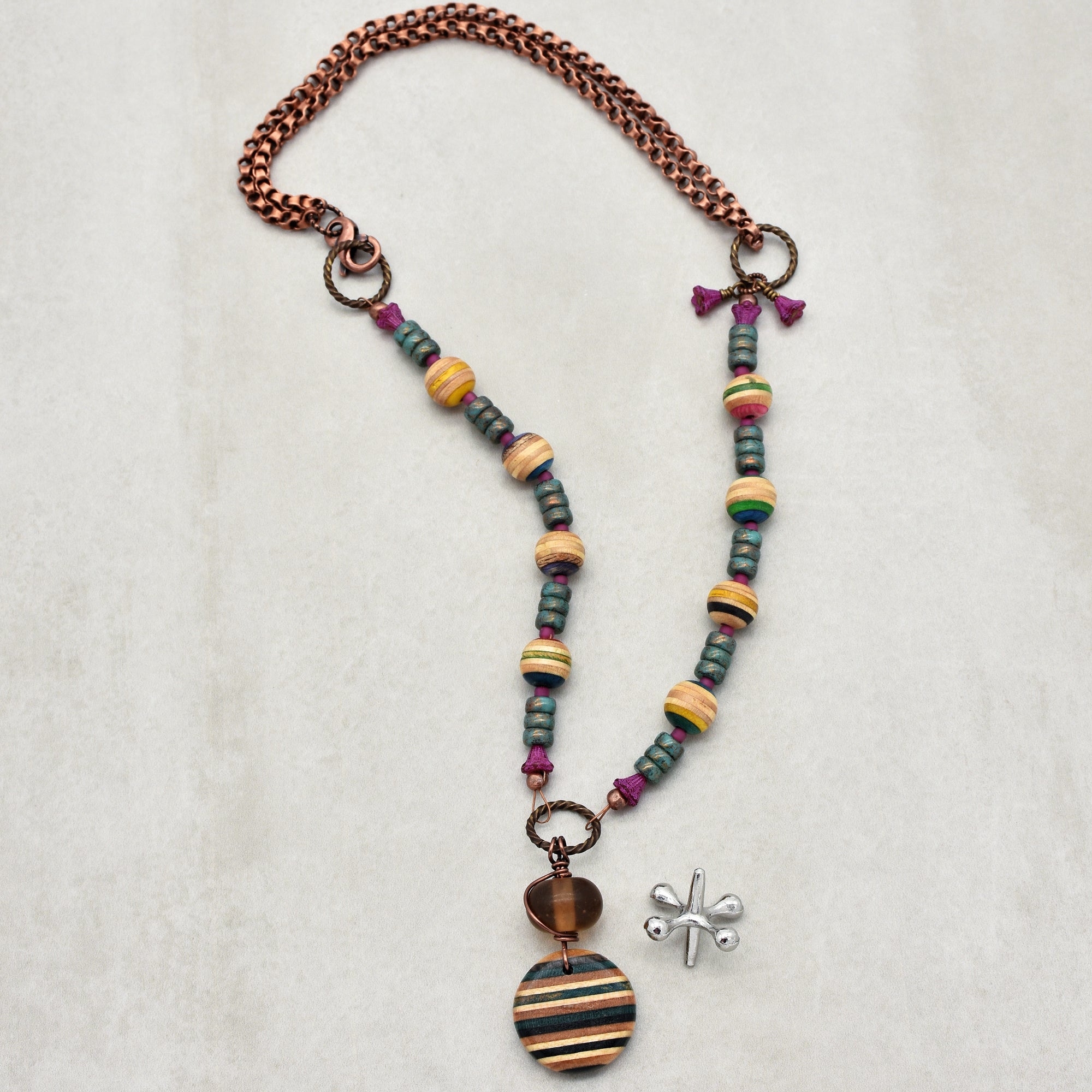This image shows a necklace. It has a chain with colorful beads and a round, striped pendant hanging from it.