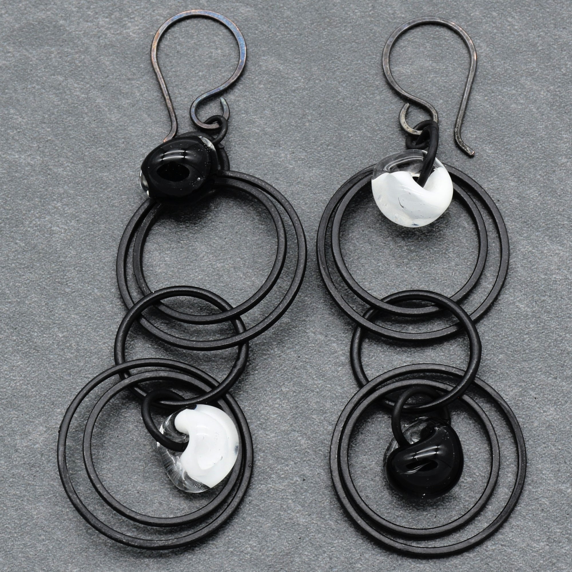 This image shows a pair of earrings. The jewelry pieces have hooks at the top for pierced ears and multiple interlinked black circular rings with decorative elements in black and white.