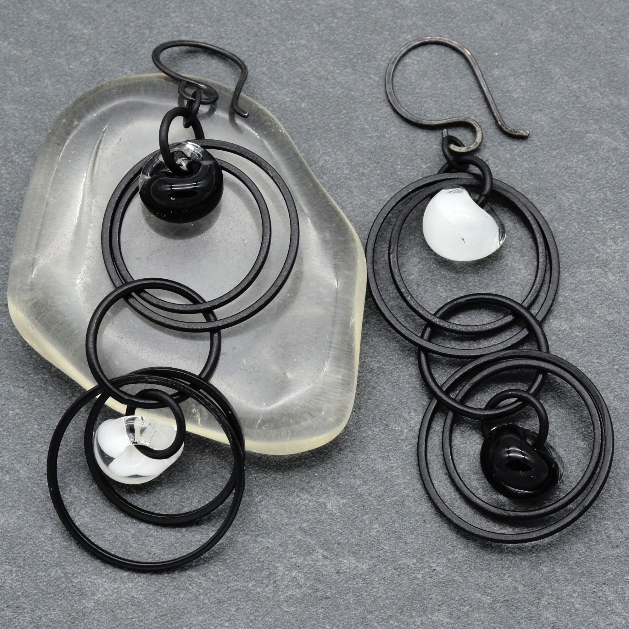 The image shows a pair of earrings. They have a design featuring multiple black circular rings with small black and white bead-like decorations attached. The hooks for wearing them are visible at the top of each piece.