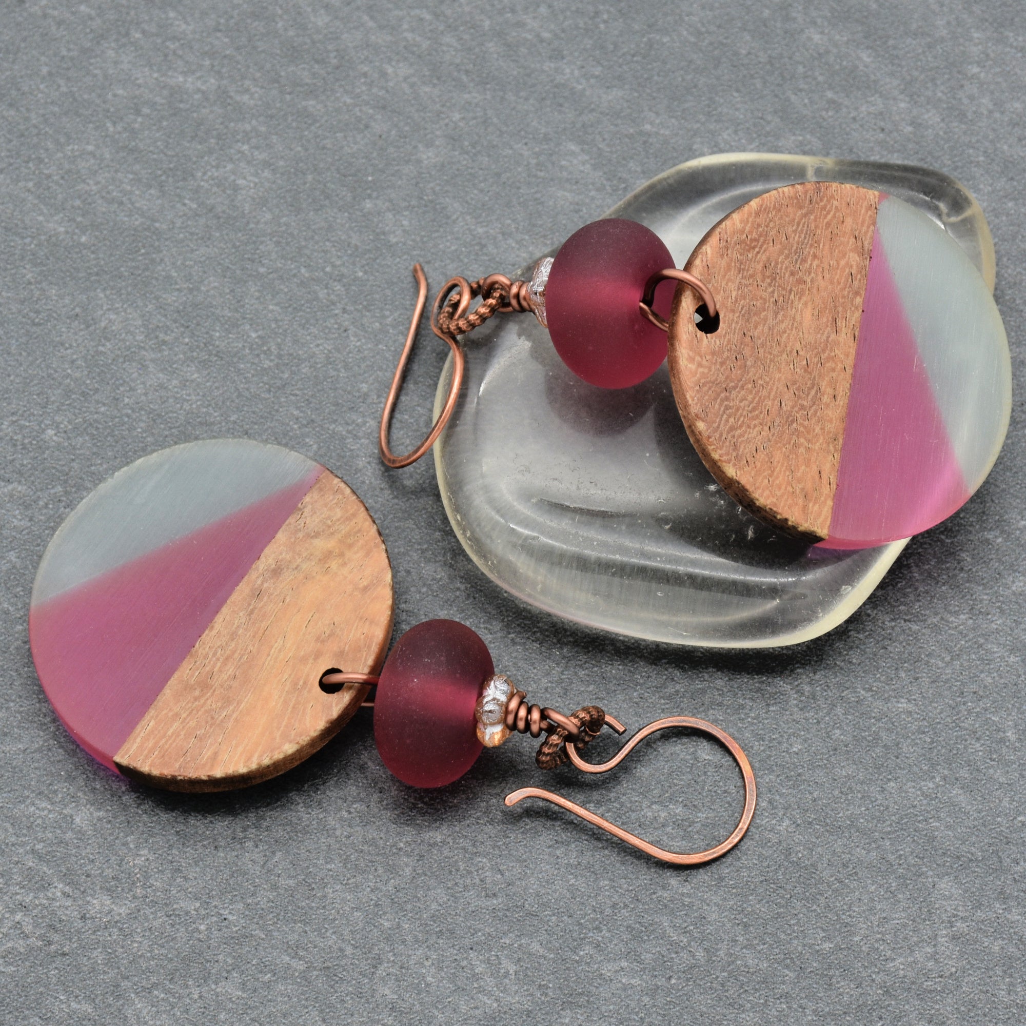 The image shows a pair of earrings. They have circular wooden and colored resin design elements, attached to copper ear hooks.
