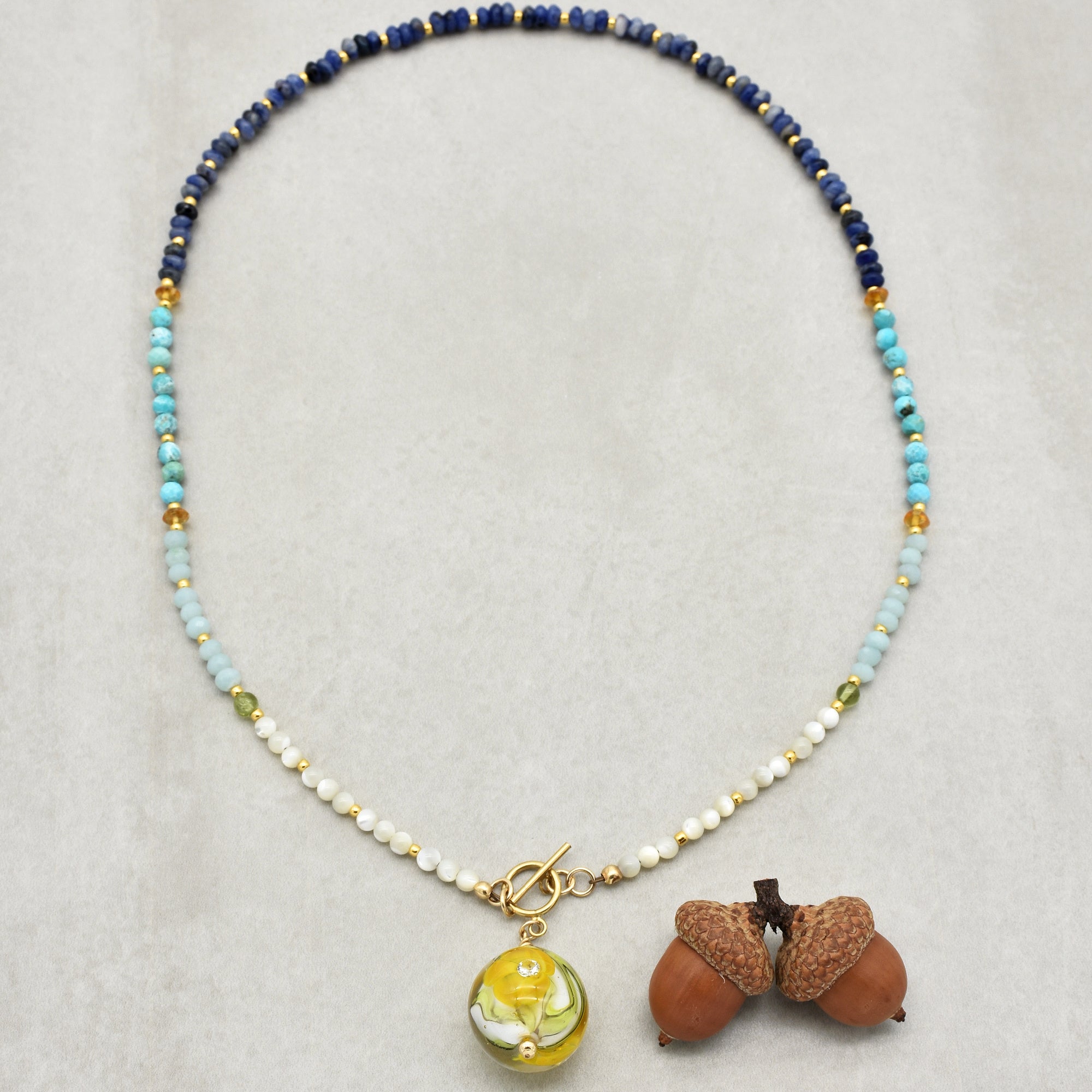 This image shows a necklace. It is made of small, colorful beads arranged in a pattern, and it has a clasp in the front along with a decorative yellow and white bead pendant. The round arrangement and clasp are typical features of a necklace.