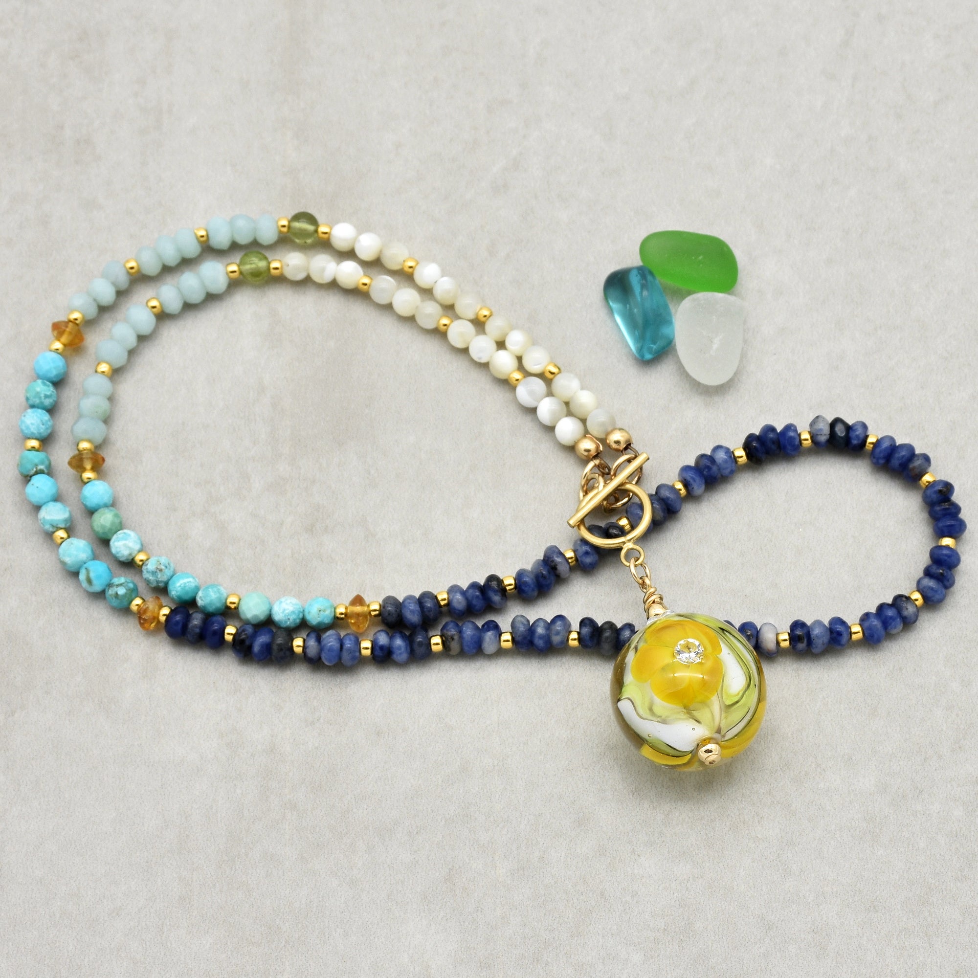 This image shows a necklace. The jewelry has a clasp and a pendant with a yellow and white flower design, which are characteristic features of a necklace.