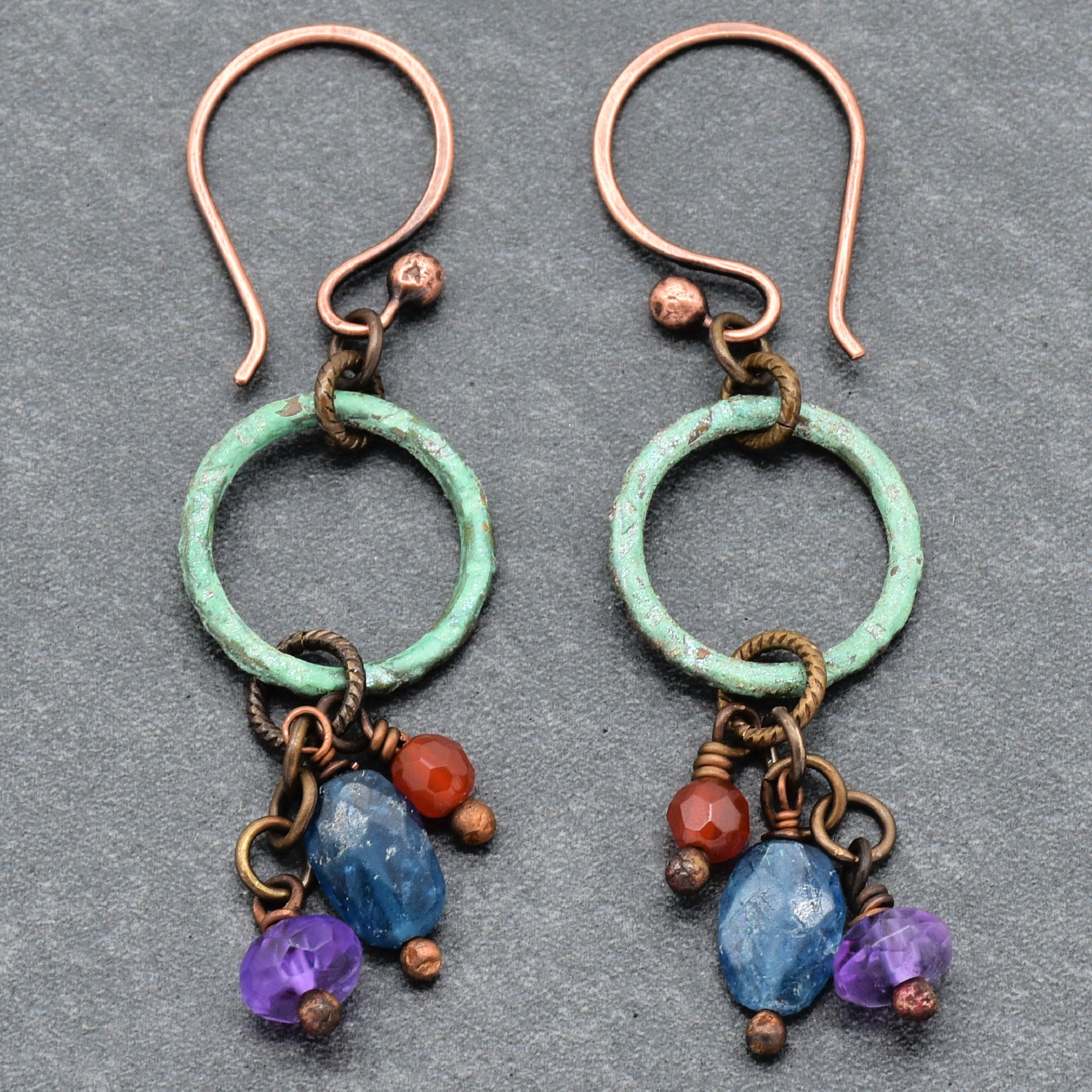 This image shows a pair of earrings. They have copper hooks and circular greenish-blue hoops with small colorful beads hanging from them.