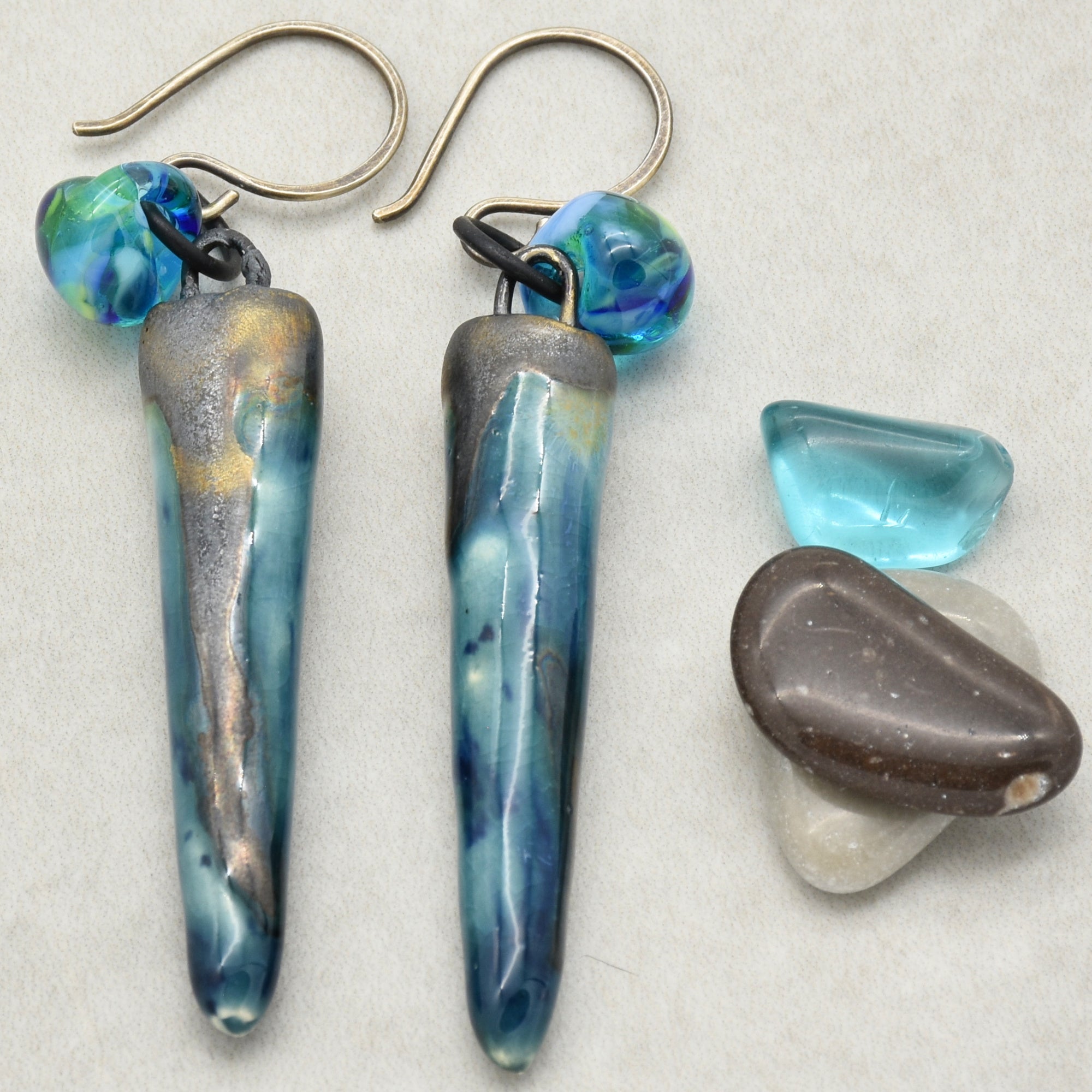 This image shows a pair of earrings. They have hooks for pierced ears and feature elongated, blue-tinted pendants with an additional blue bead near the hook.