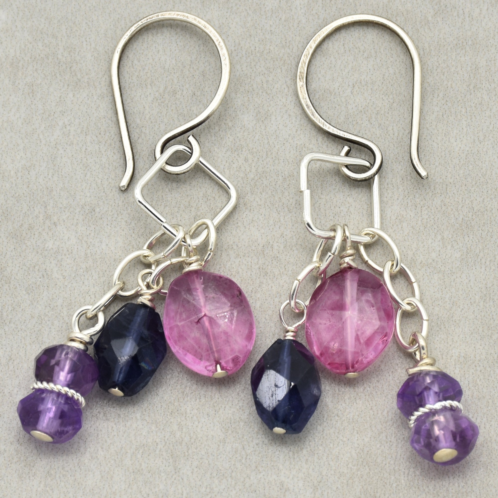 The image shows a pair of earrings. The jewelry pieces have hooks for wearing in pierced ears and feature decorative beads in pink, purple, and dark blue colors.