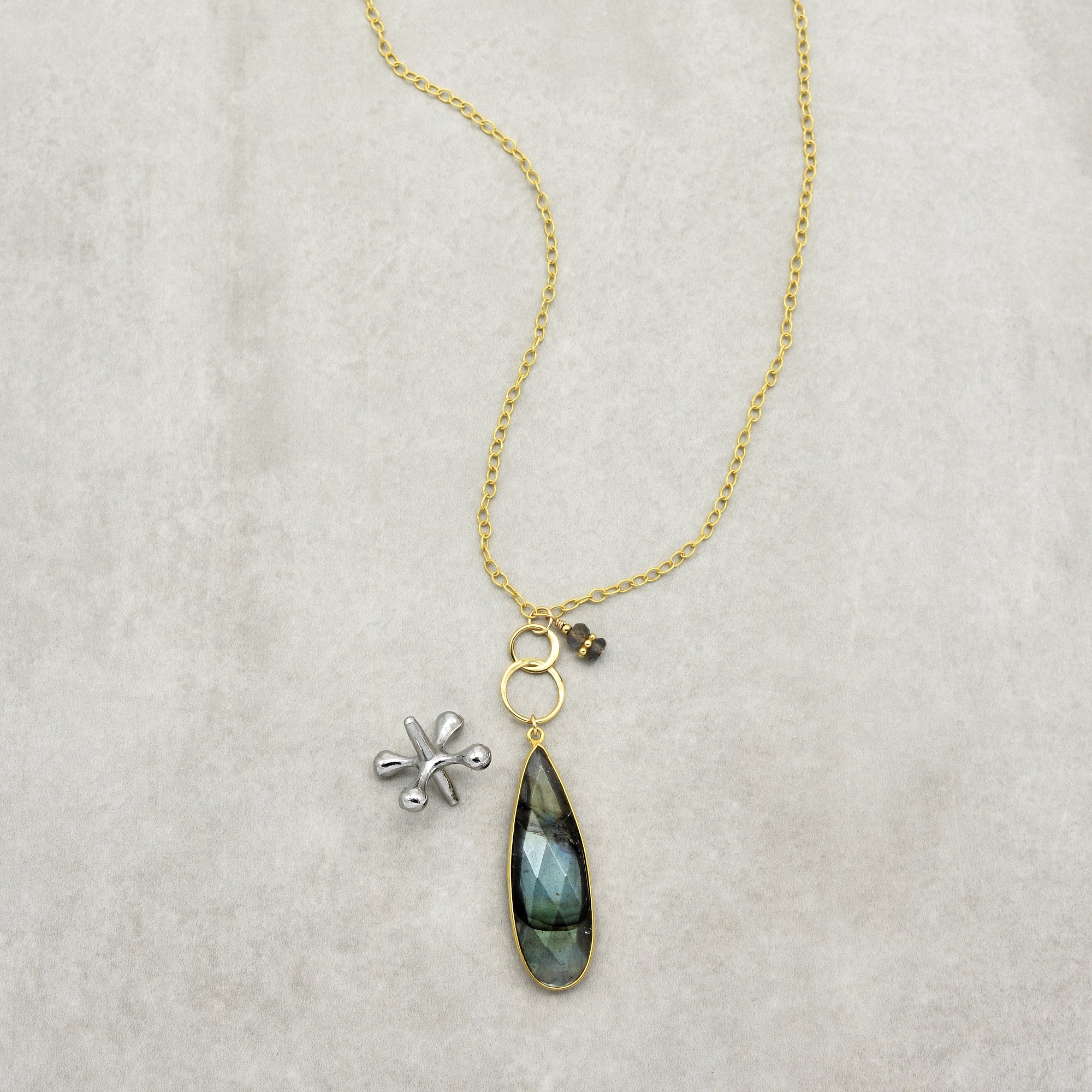 This image shows a necklace. It has a gold chain with a pendant that includes a teardrop-shaped stone and some small decorative elements.