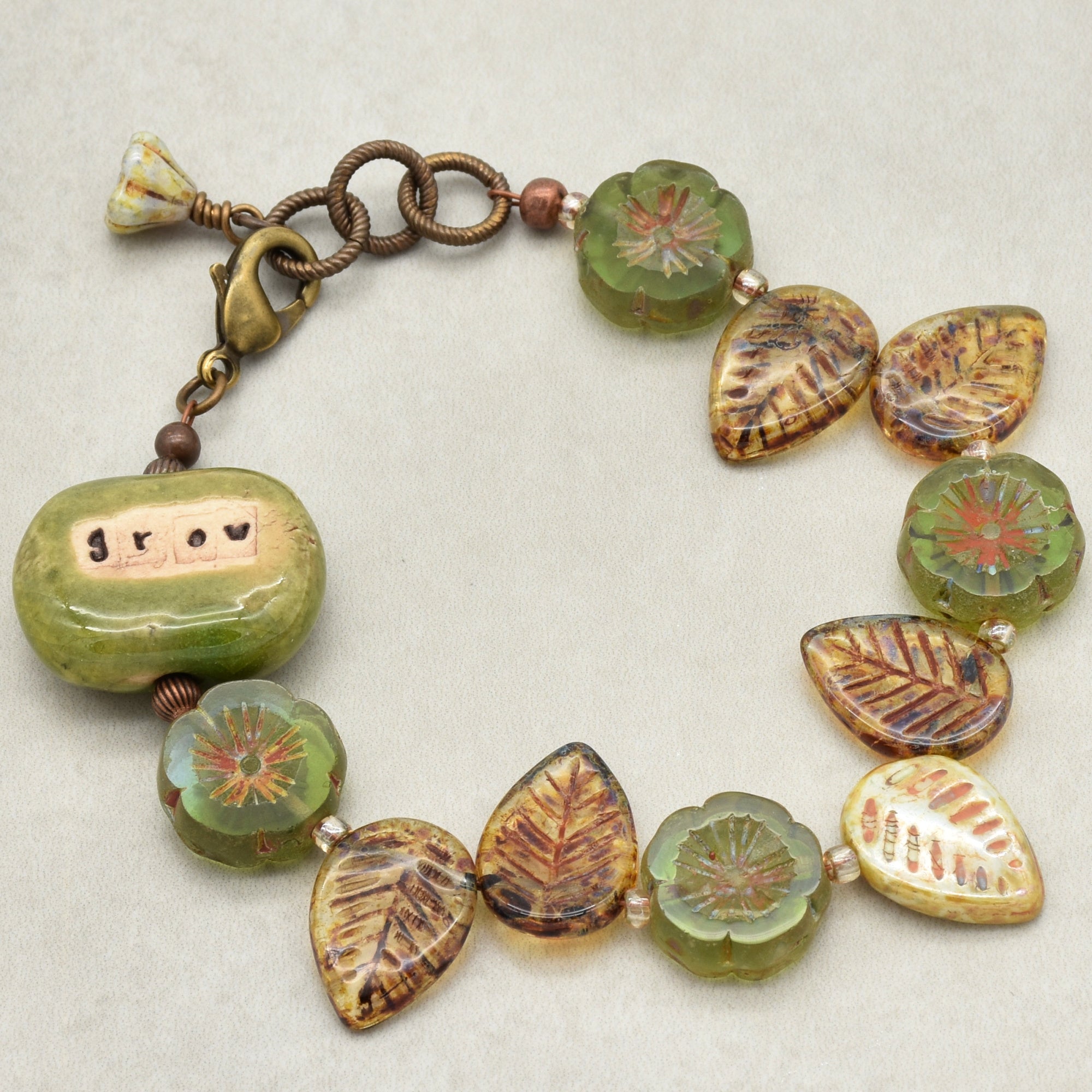 This image shows a bracelet. It features a clasp and an adjustable chain, along with decorative beads shaped like leaves and flowers, in earthy tones of green and brown.
