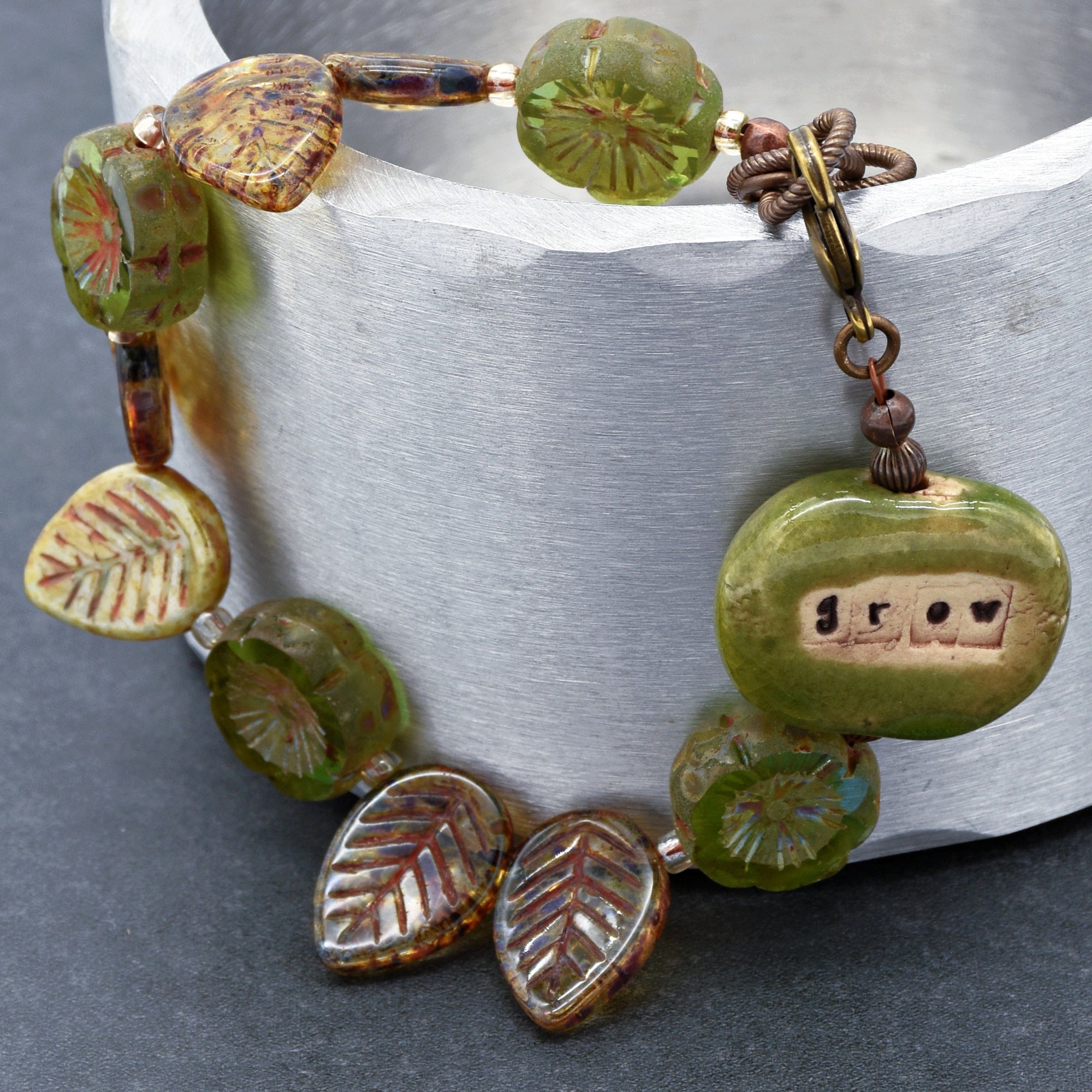 The jewelry shown in the image is a bracelet. It has a circular shape suitable for wearing around the wrist, and it is made of various decorative beads and a clasp. One of the beads has the word "grow" inscribed on it.